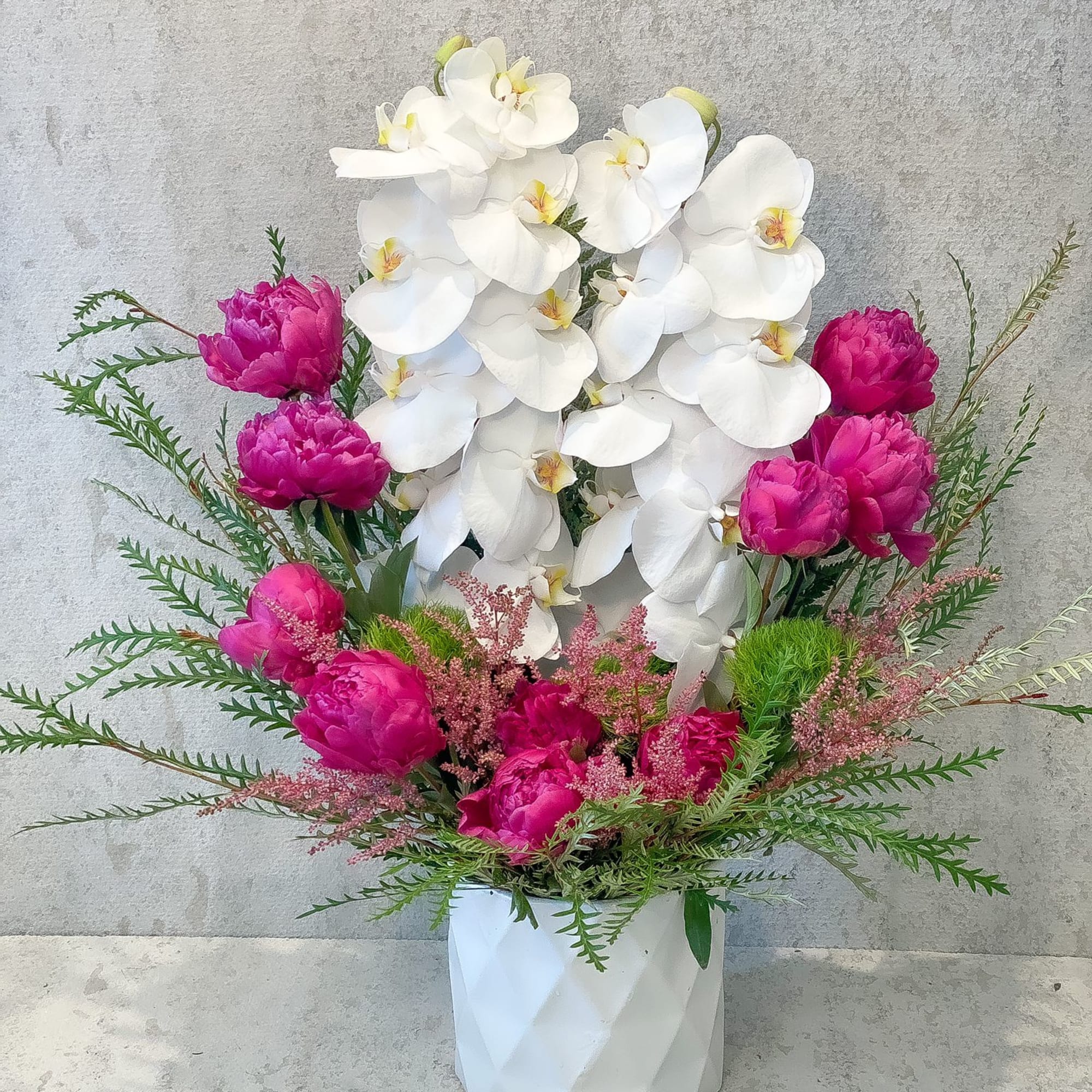 White orchids and bright pink peonies in a white vase