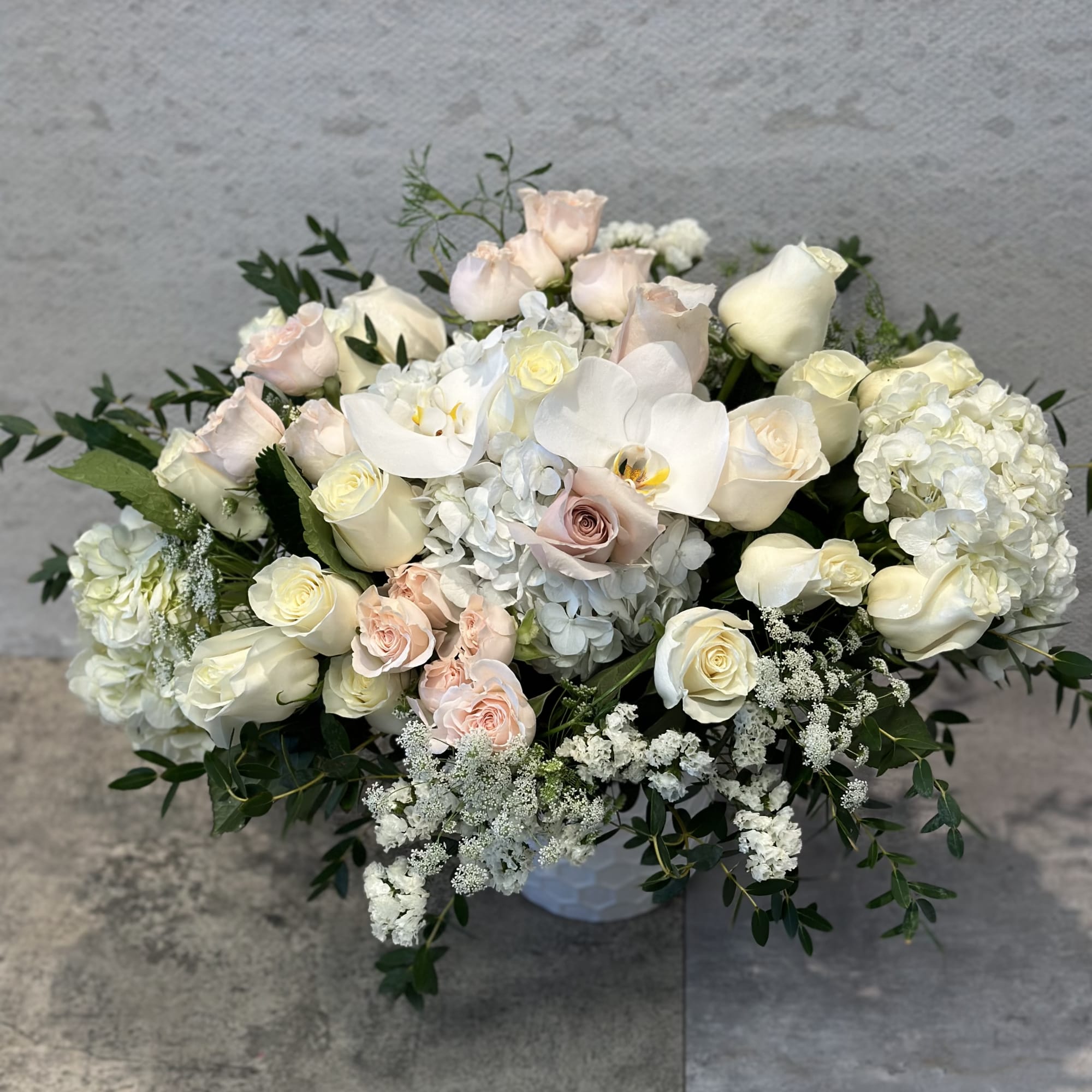 Low bouquet of white and blush roses with white orchids in a vase