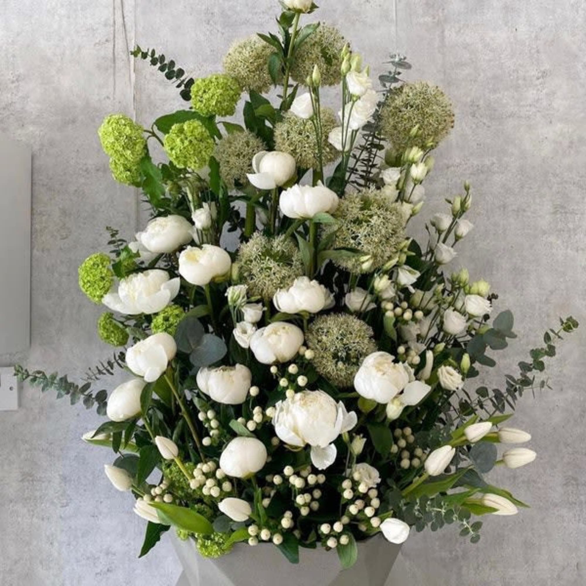 Tall white floral arrangement with green accents in a gray container