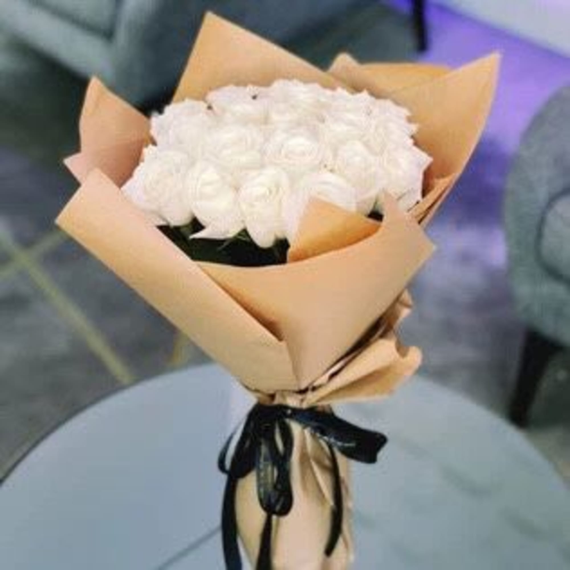 Bouquet of white roses wrapped in tan paper with a black ribbon