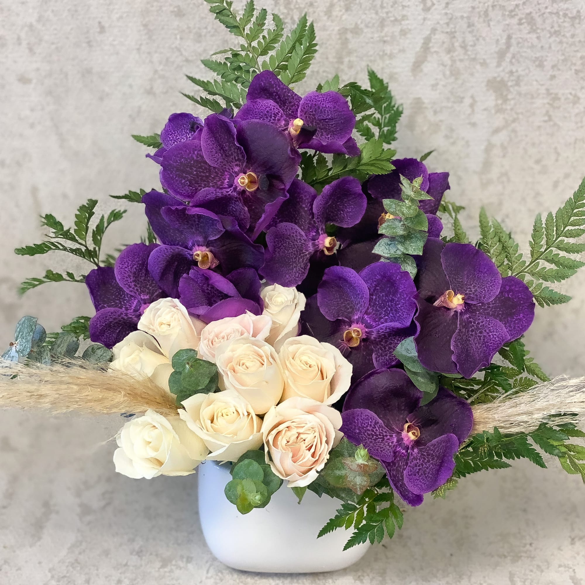 Purple orchids and cream roses in a white vase