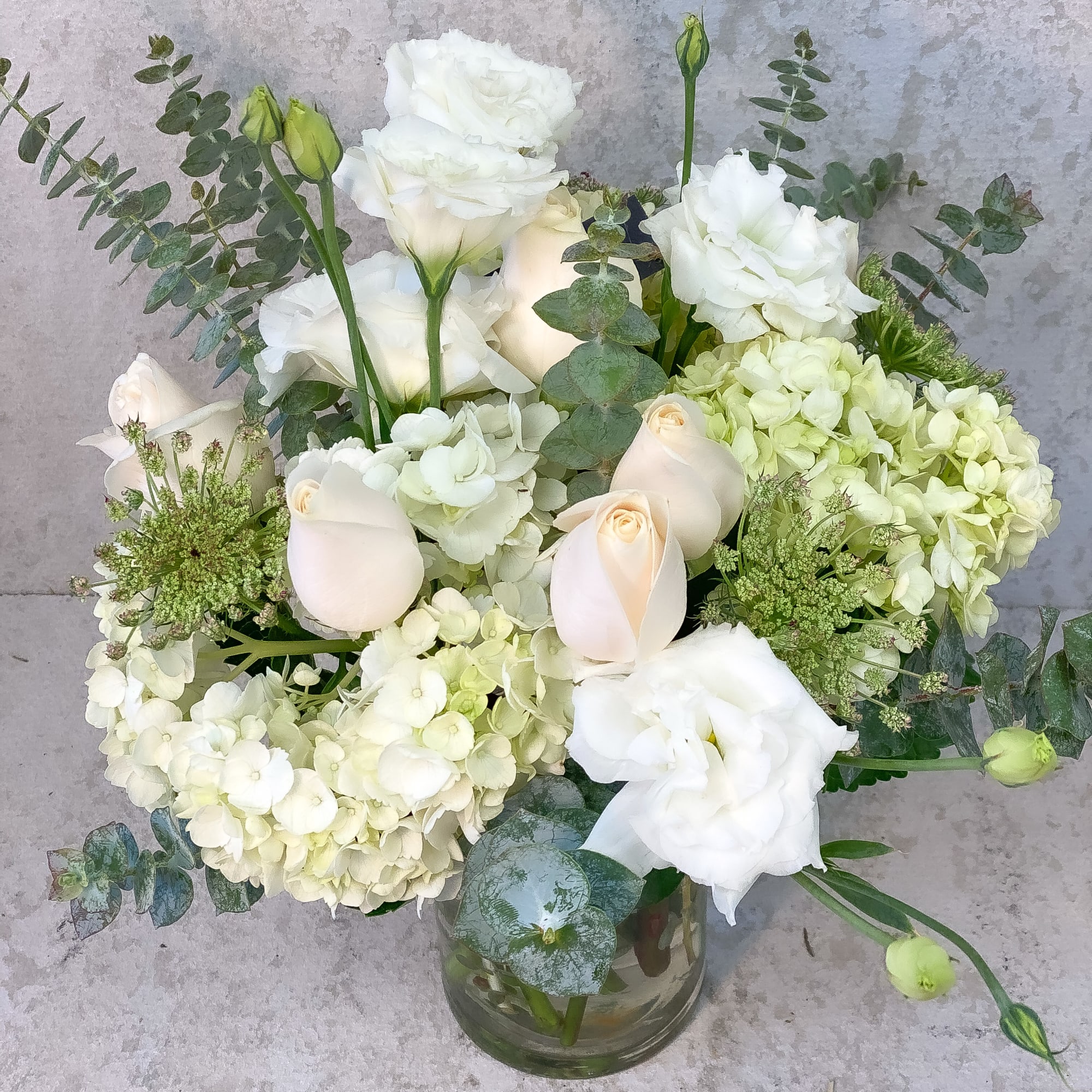 White floral arrangement in a glass vase with hydrangeas and roses