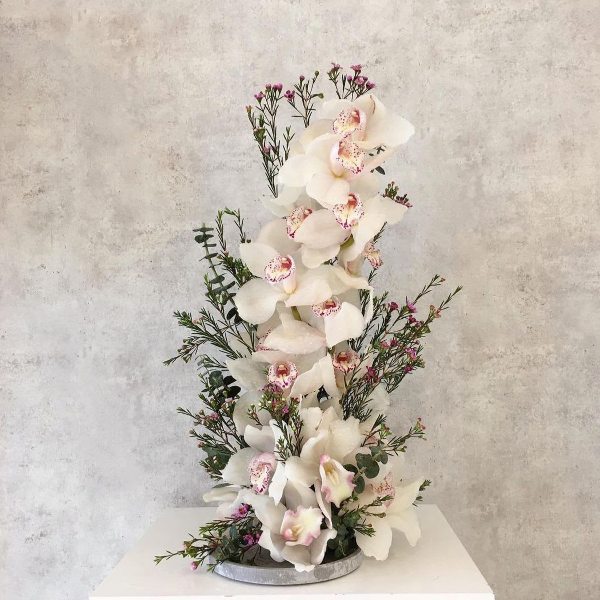 Tall white orchid arrangement with small pink accent flowers in a round base