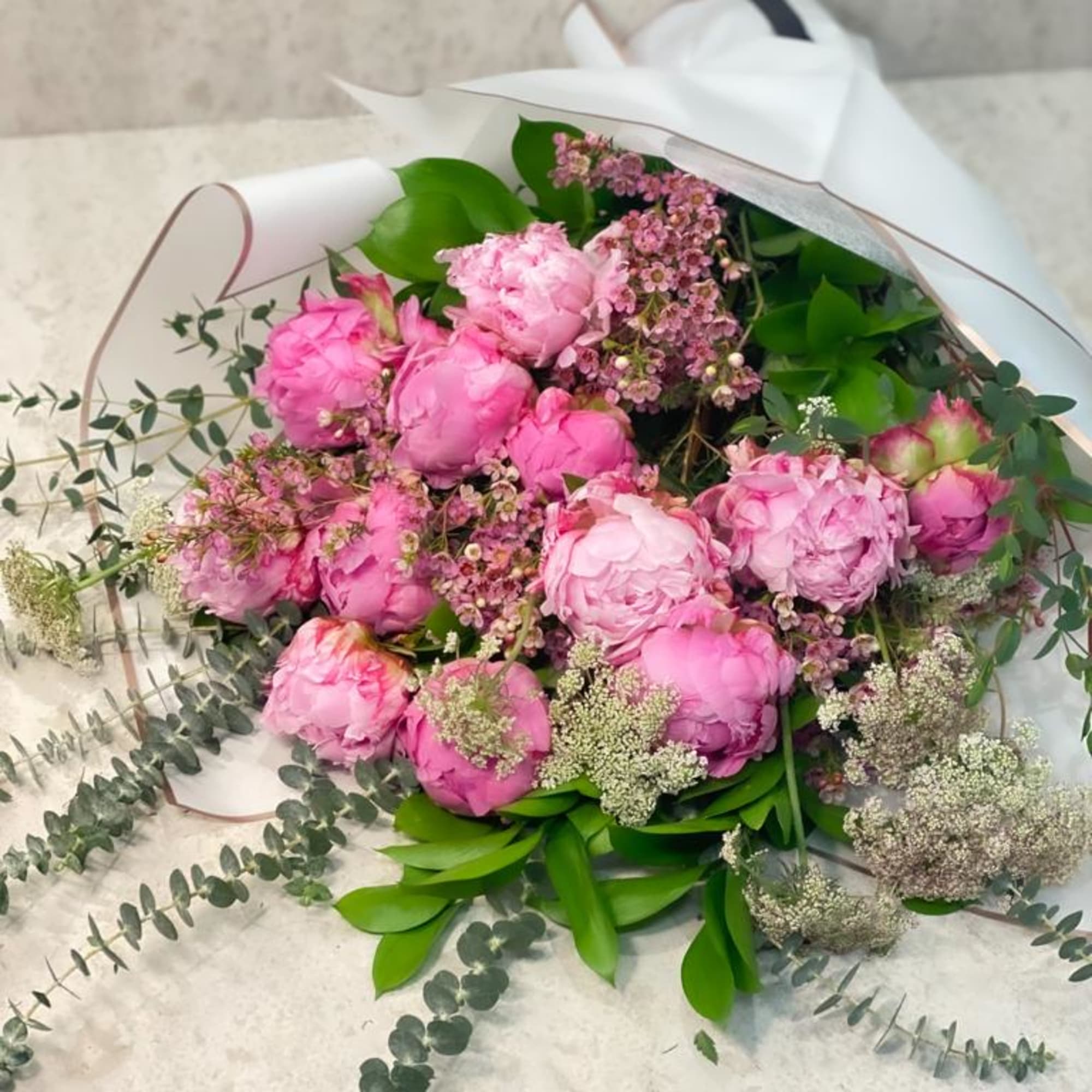 Pink peony bouquet wrapped in white paper with greenery