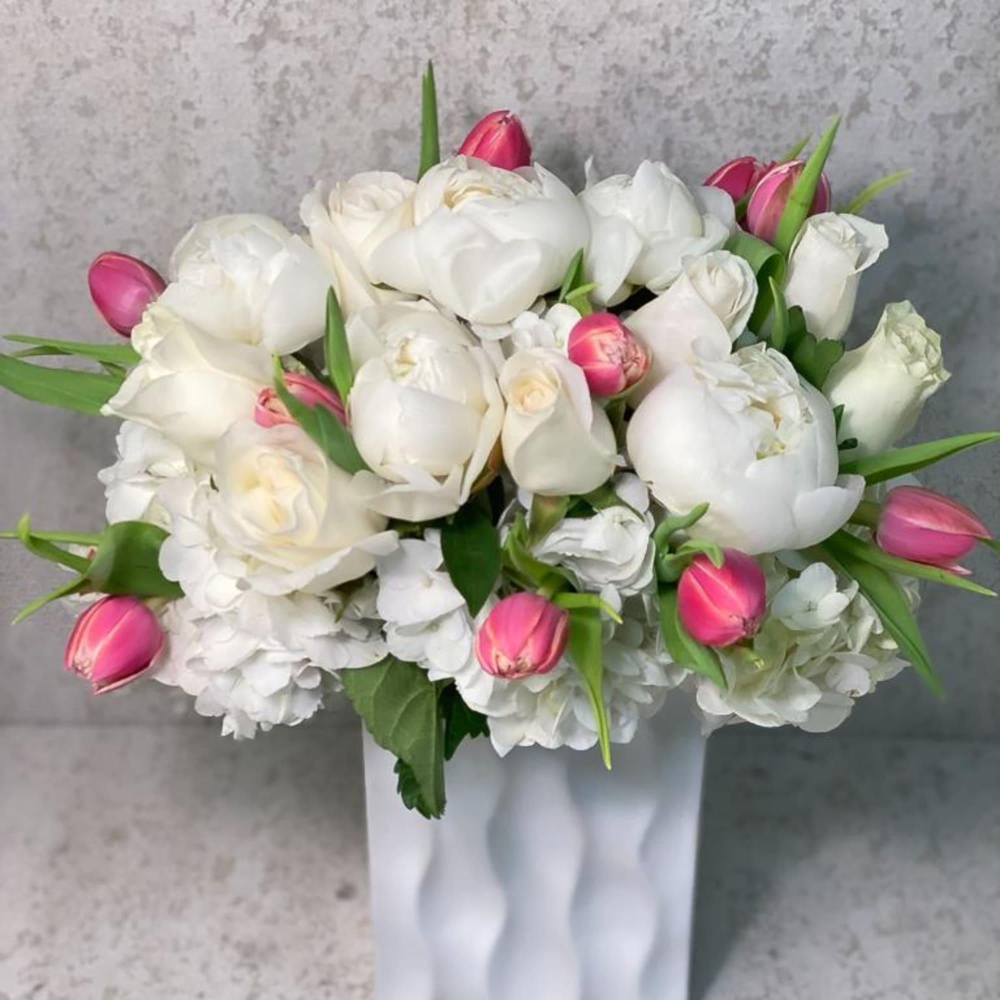 White tulips and roses arranged in a white vase with pink tulip buds