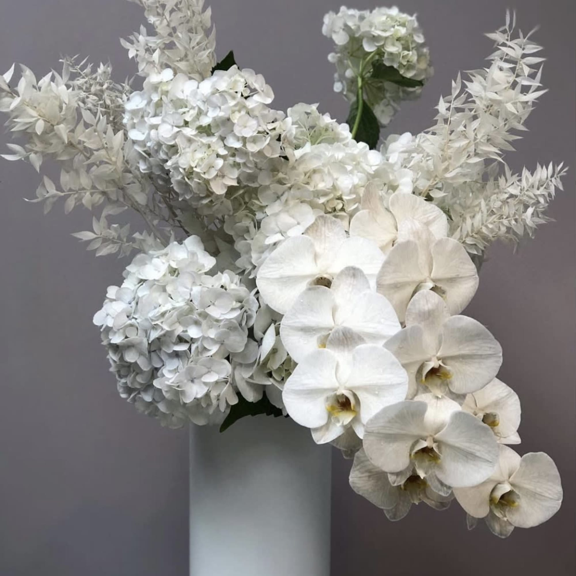 White hydrangeas and orchids arranged in a tall vase