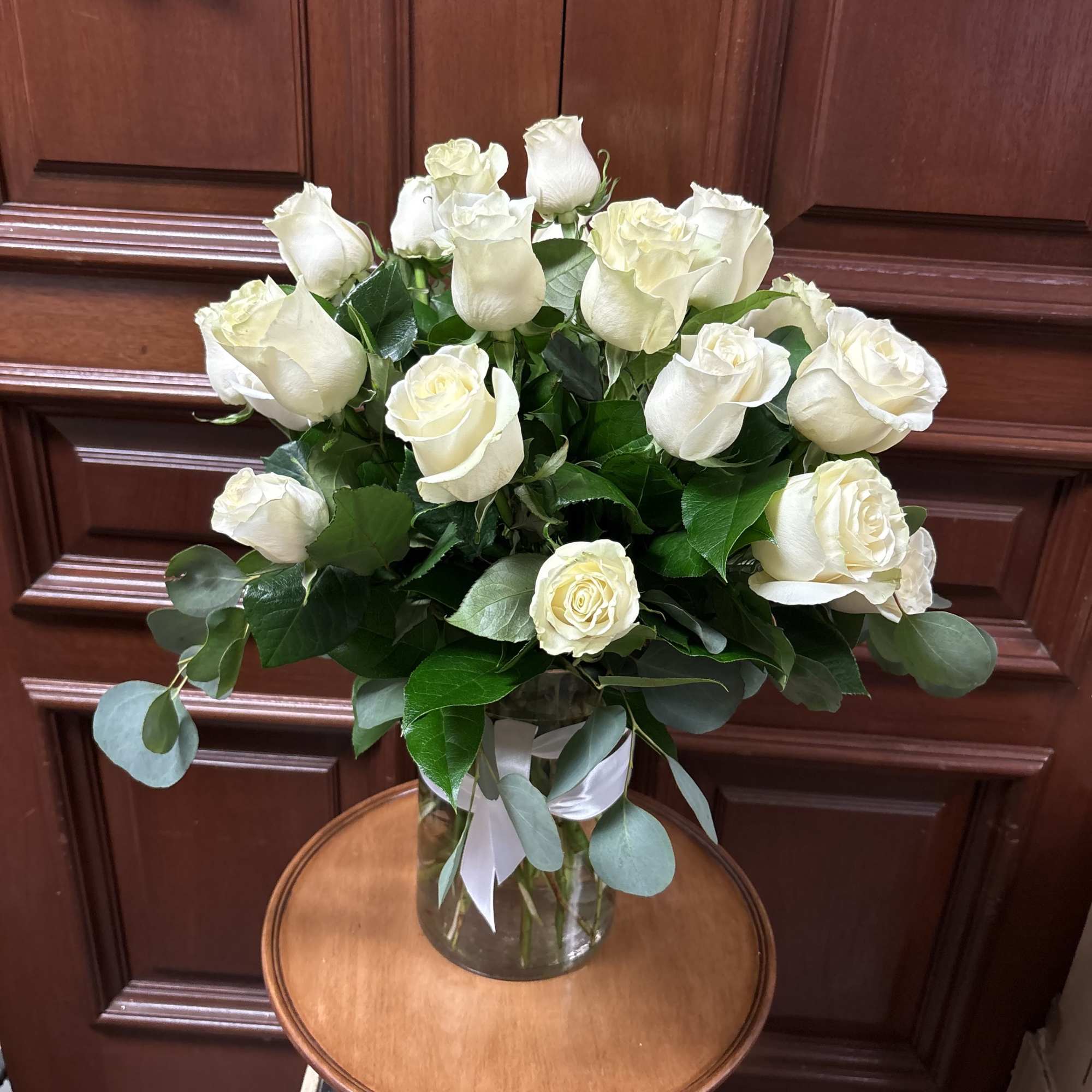 Arrangement of cream roses in a clear glass vase with a white ribbon bow