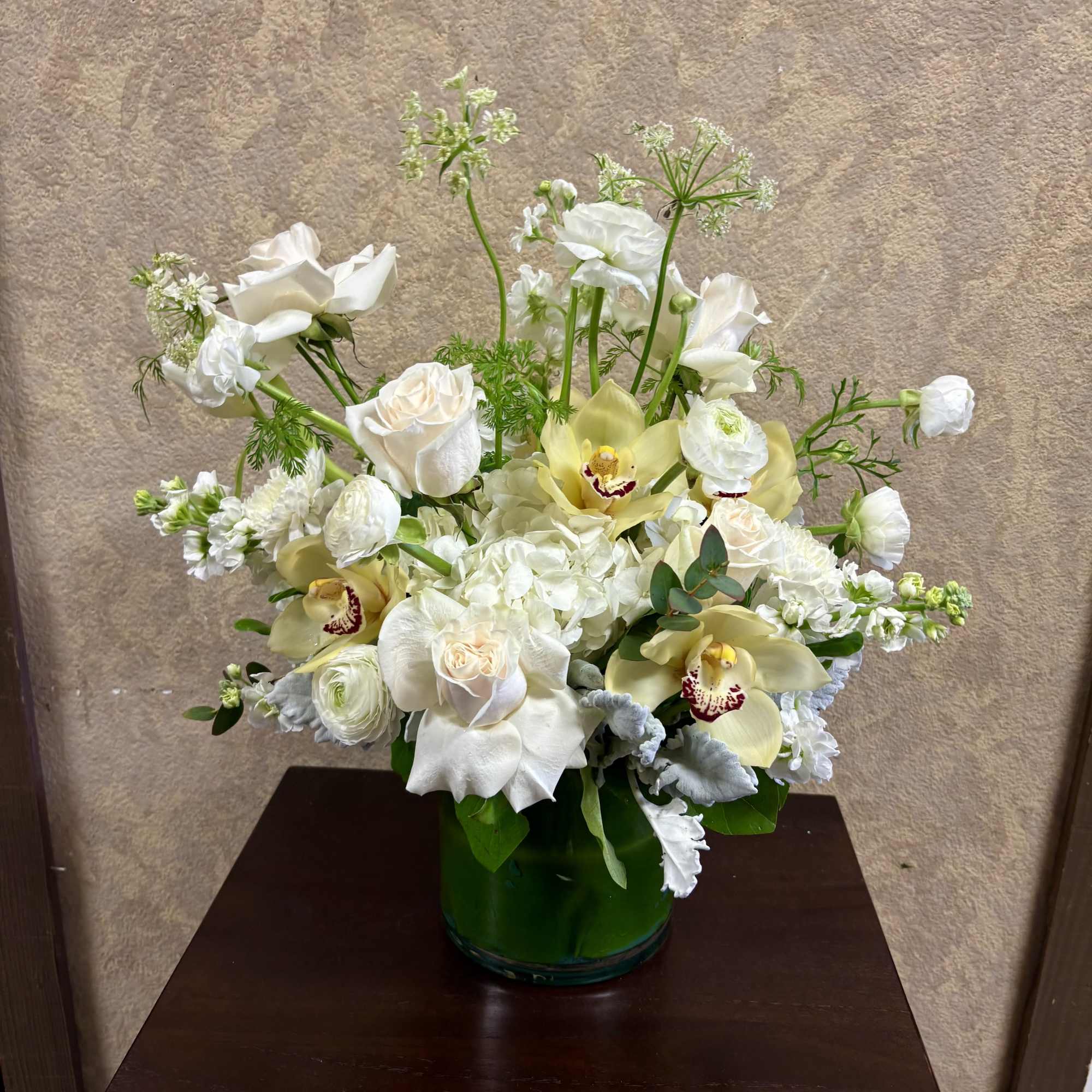 White roses and orchids arranged in a green glass vase