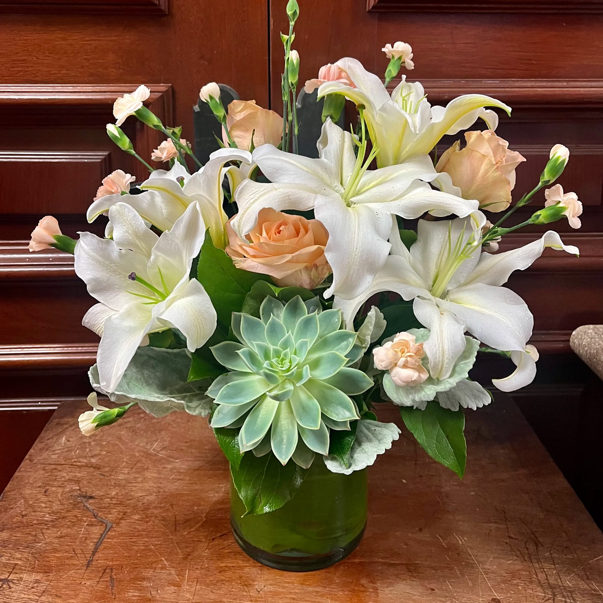 White lilies and peach roses in a green glass vase with a succulent accent