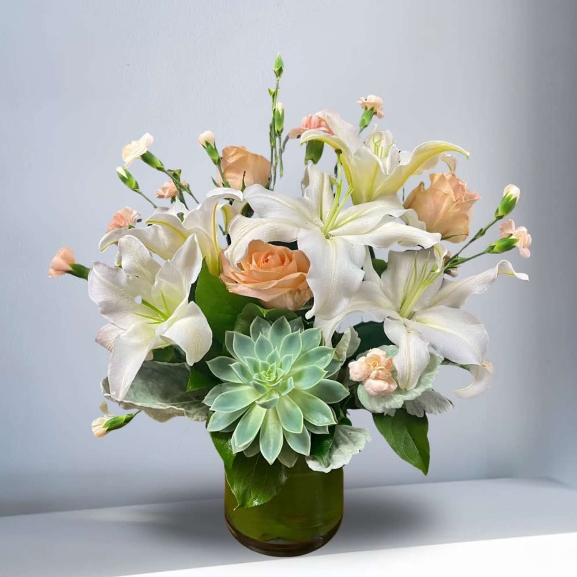 White lilies and peach roses in a green glass vase with a succulent accent
