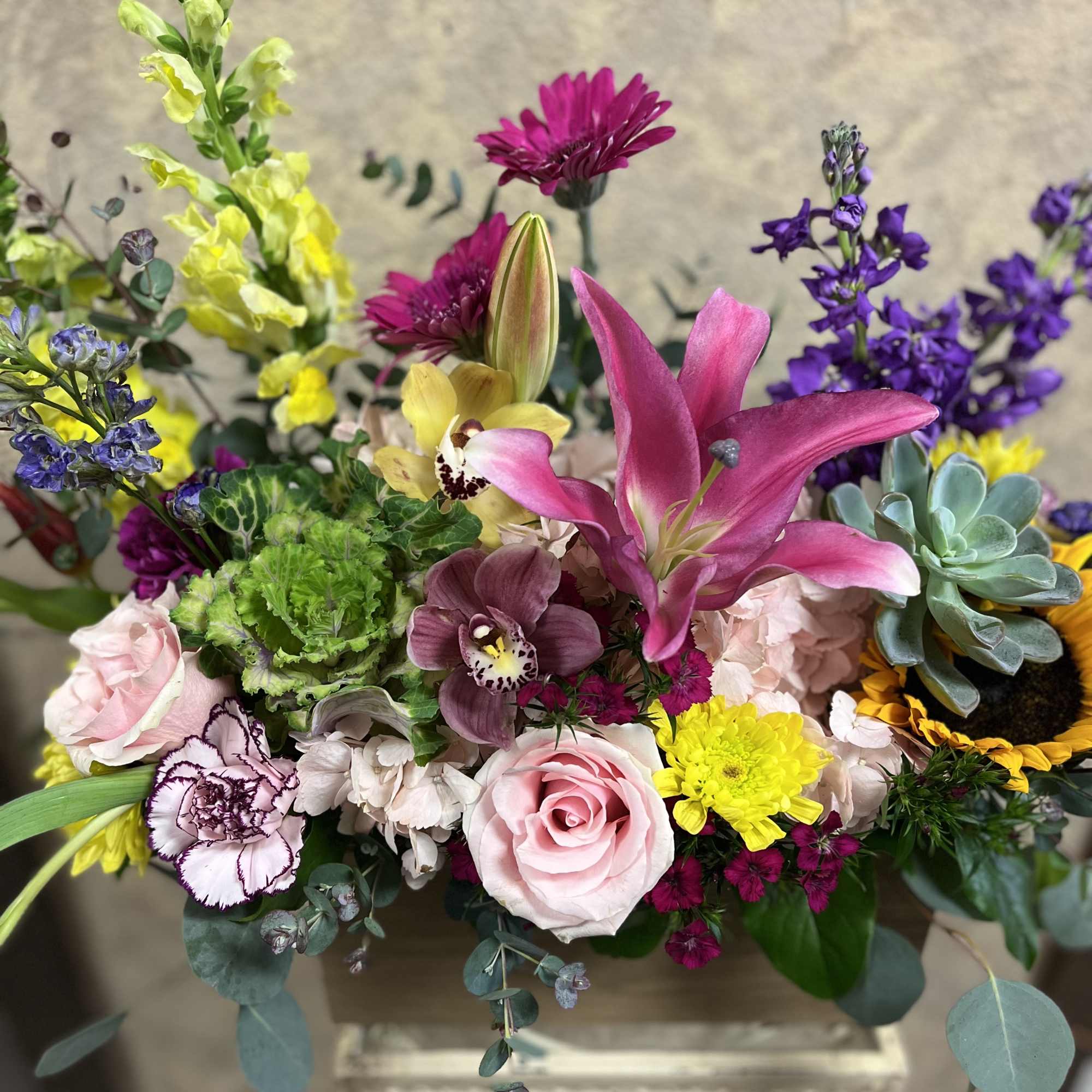 Colorful arrangement with pink lilies, roses, orchids, succulents and mixed blooms in a low container