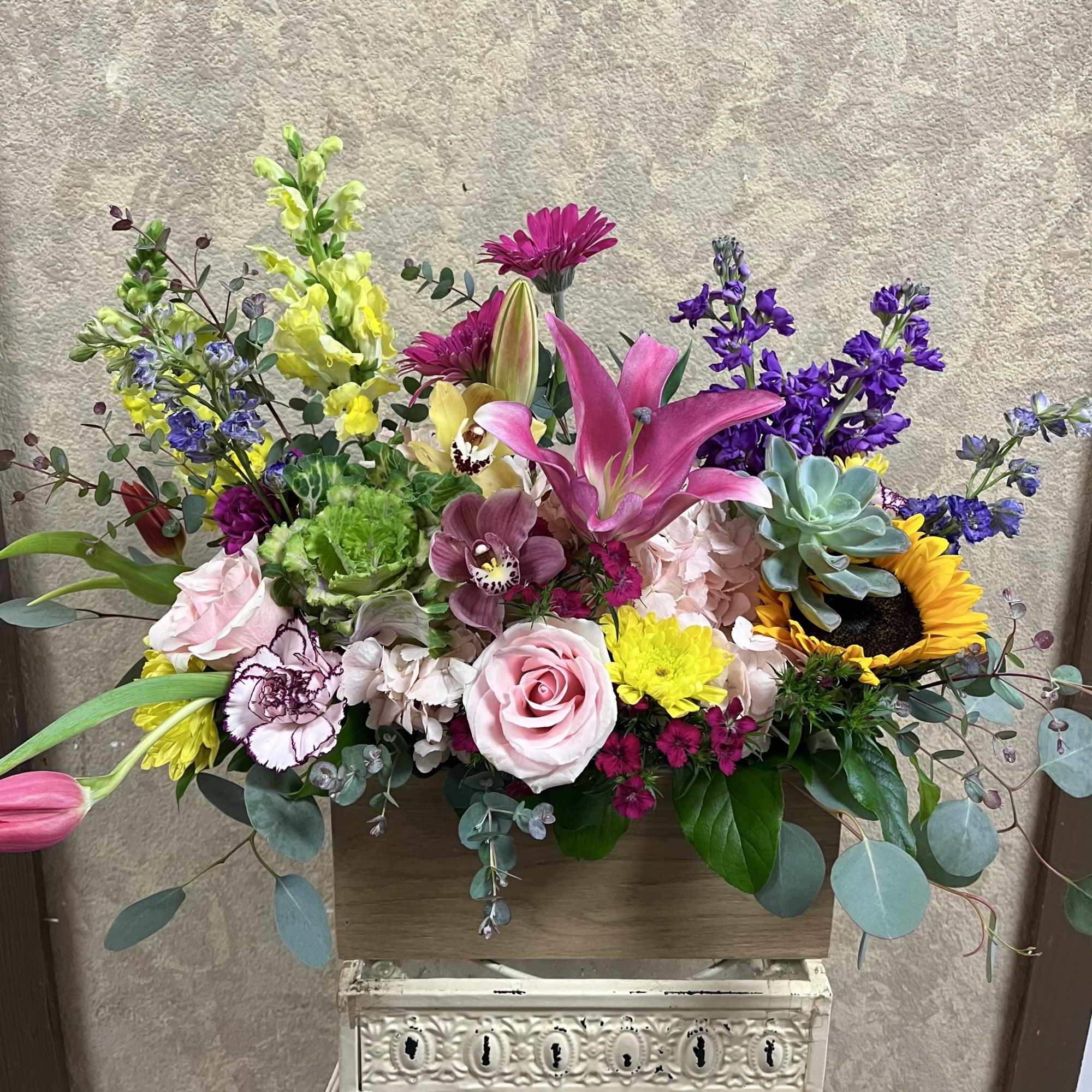 Colorful mixed flower arrangement with lilies, roses, orchids, succulents and a sunflower in a wooden box