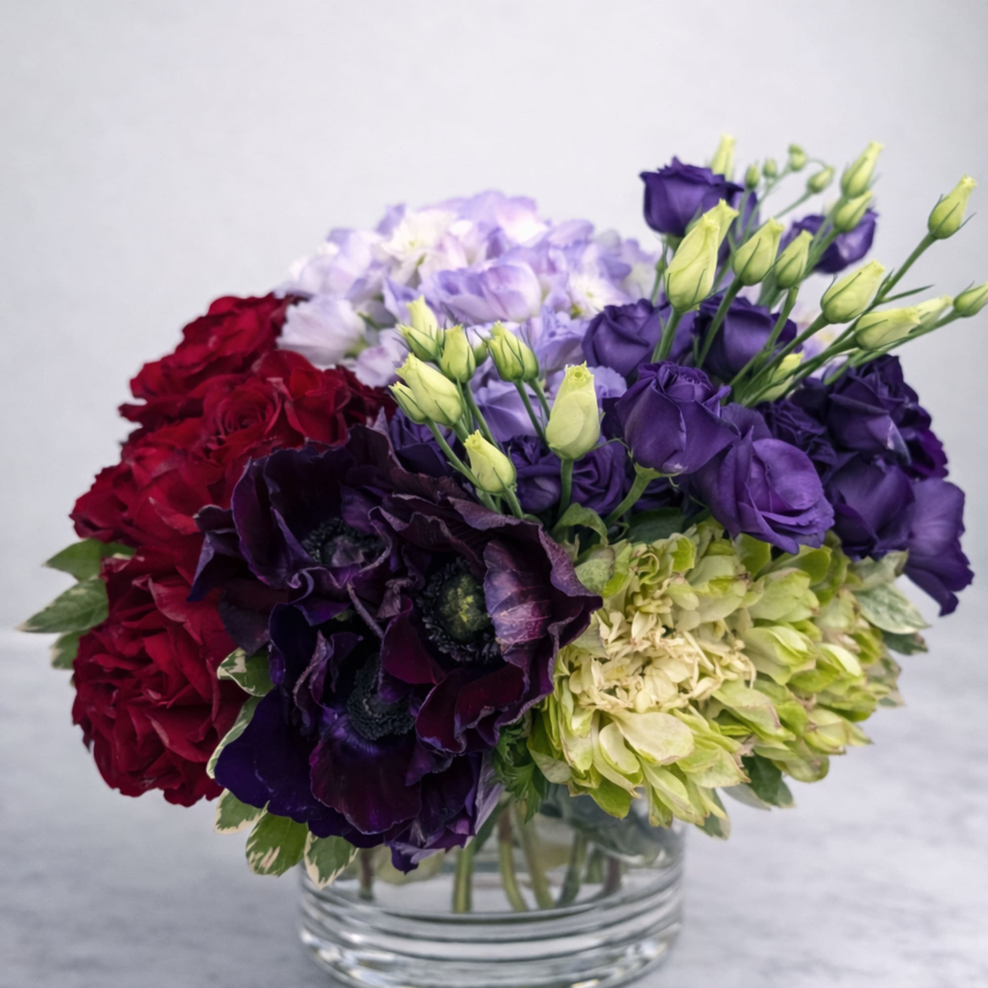 Mixed bouquet of purple, red, and green flowers in a clear glass vase
