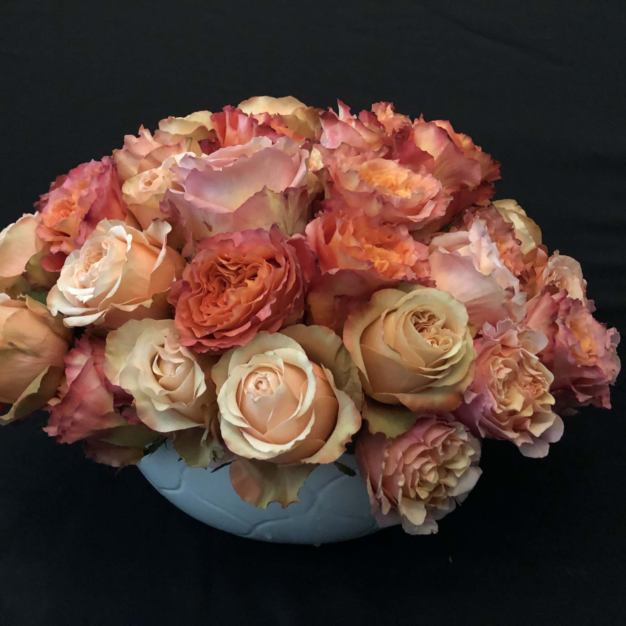Peach and pink roses arranged in a low white bowl