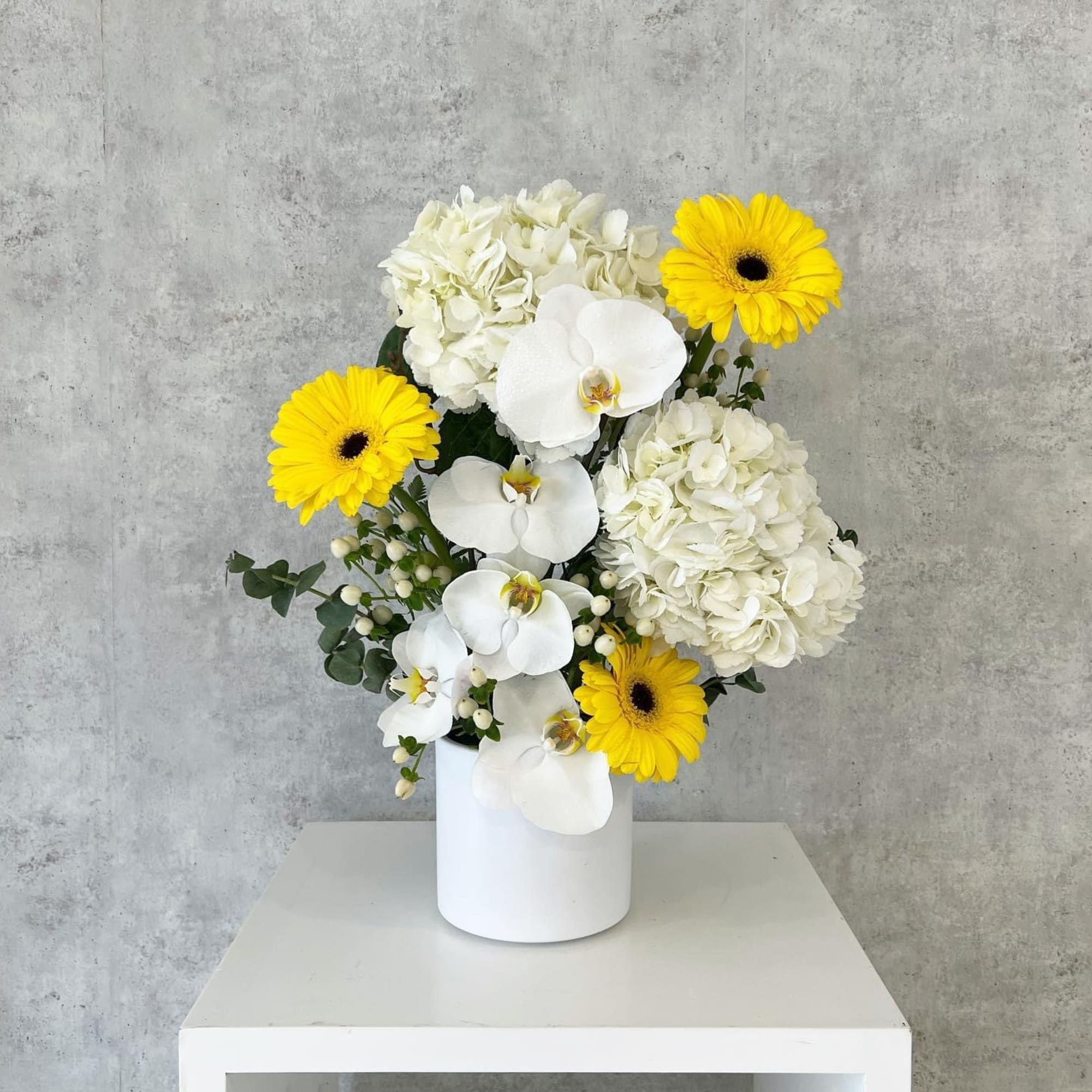 White orchids, hydrangeas, and yellow gerbera daisies in a white vase