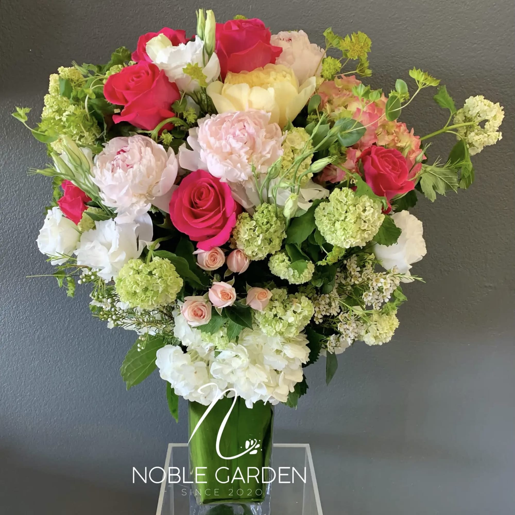 Mixed bouquet of pink, white, and green flowers in a tall glass vase