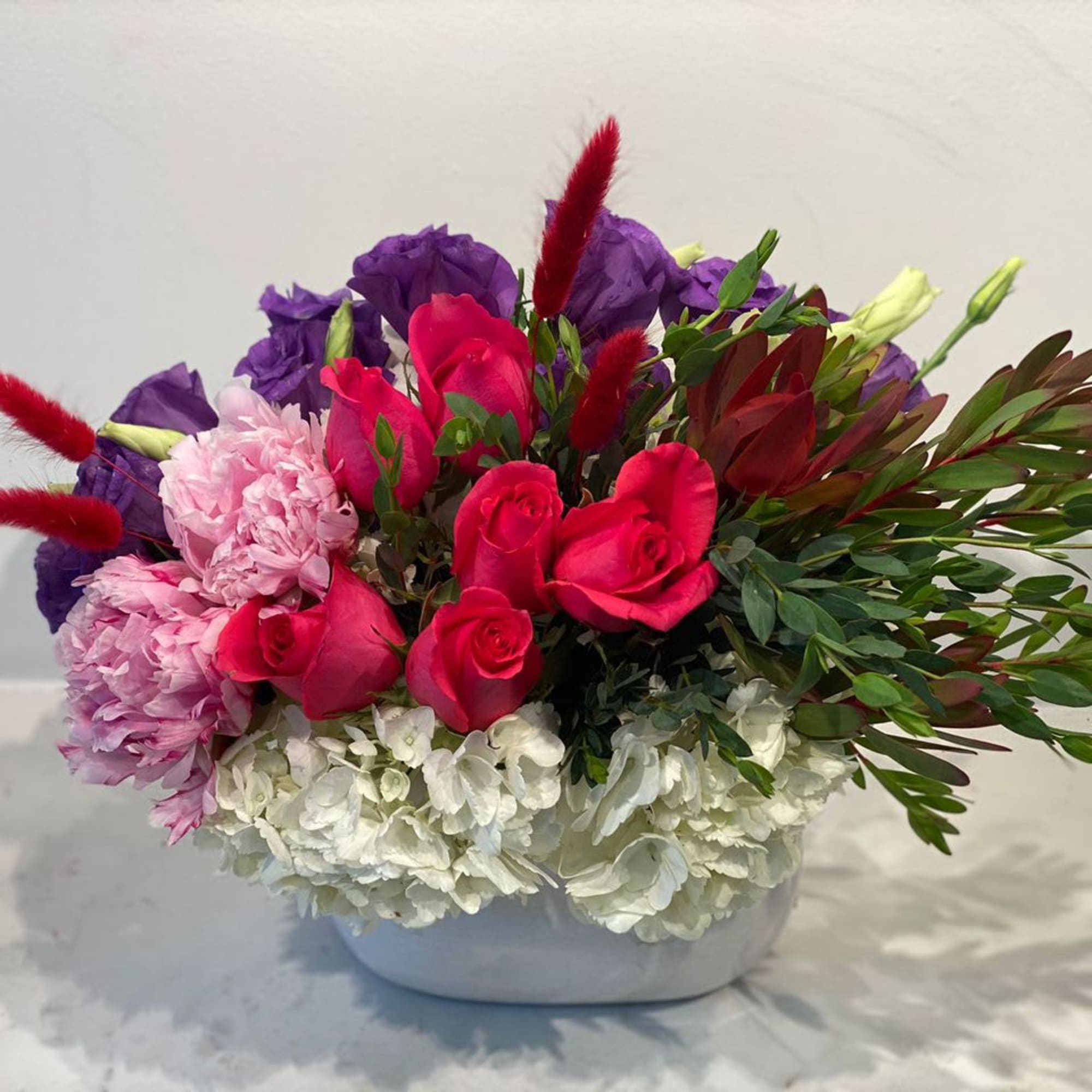 Bouquet of pink roses, purple blooms, and white flowers in a white vase