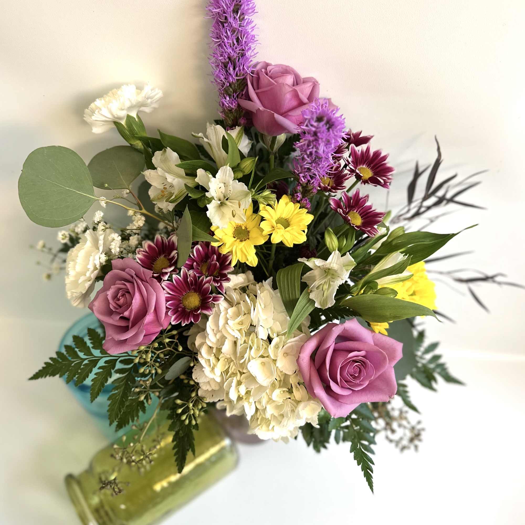 Mixed bouquet of pink roses, white blooms, and yellow daisies in a glass vase