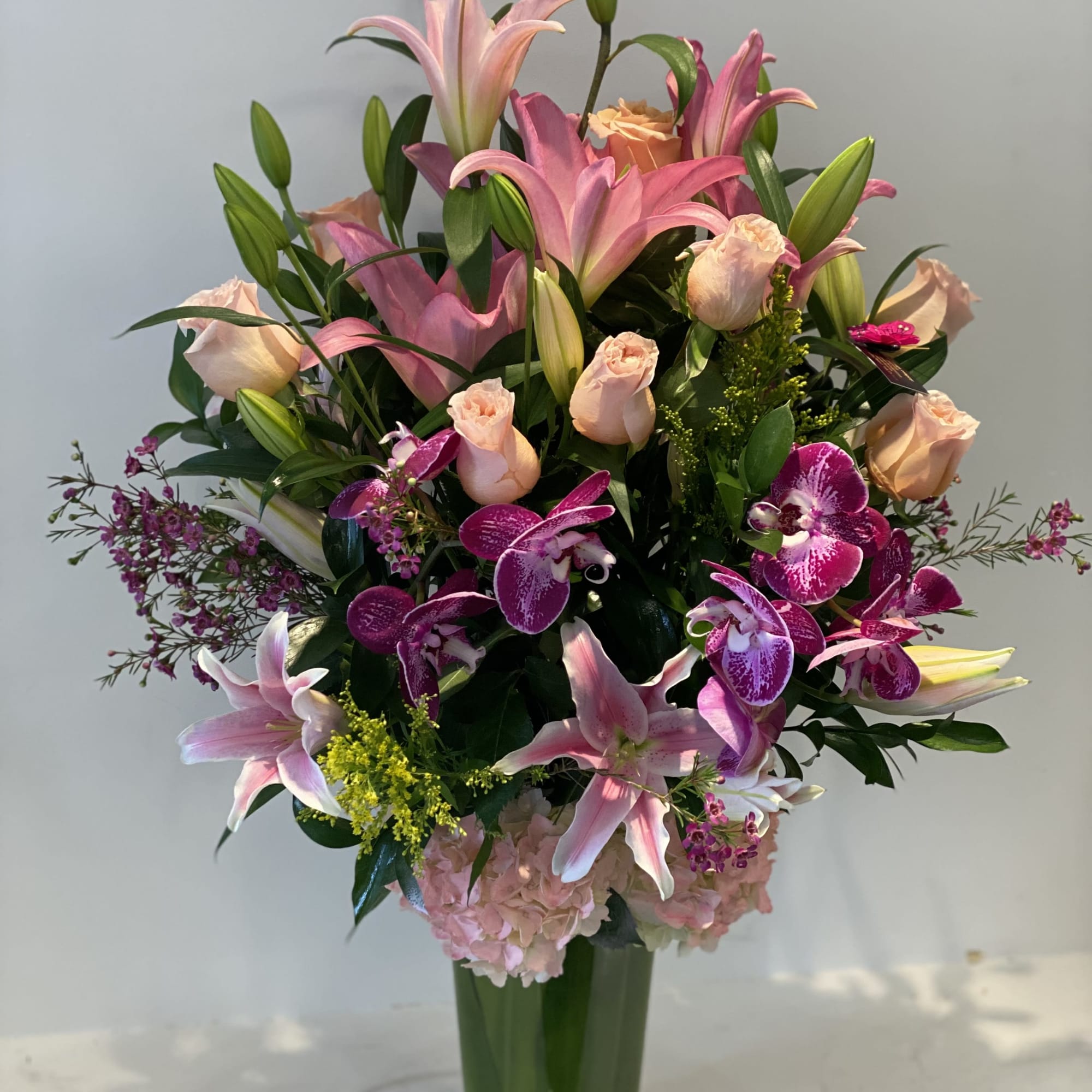 Pink lilies, roses, and orchids arranged in a tall glass vase