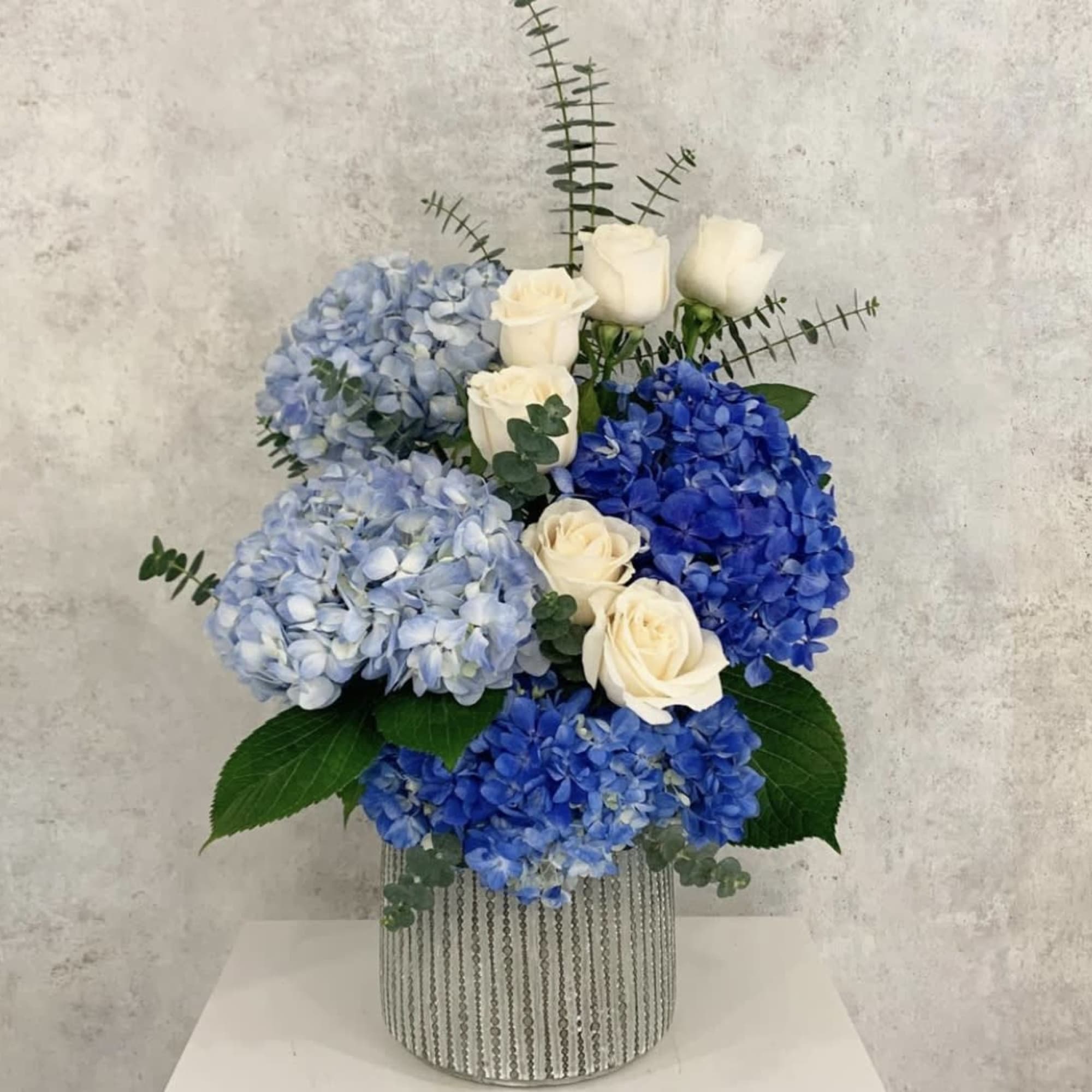 Blue hydrangeas and white roses in a silver striped vase