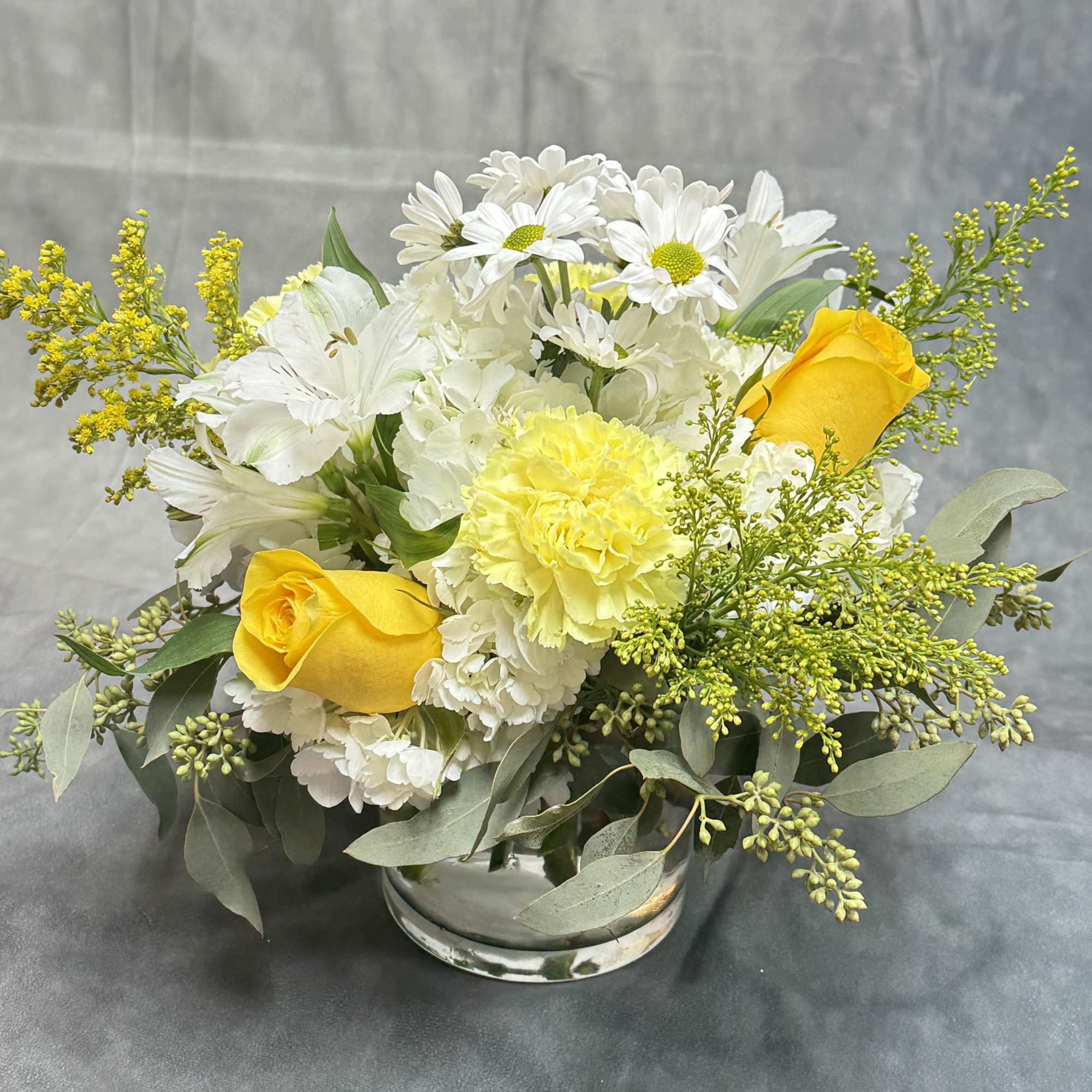 Yellow roses and white daisies in a low glass vase