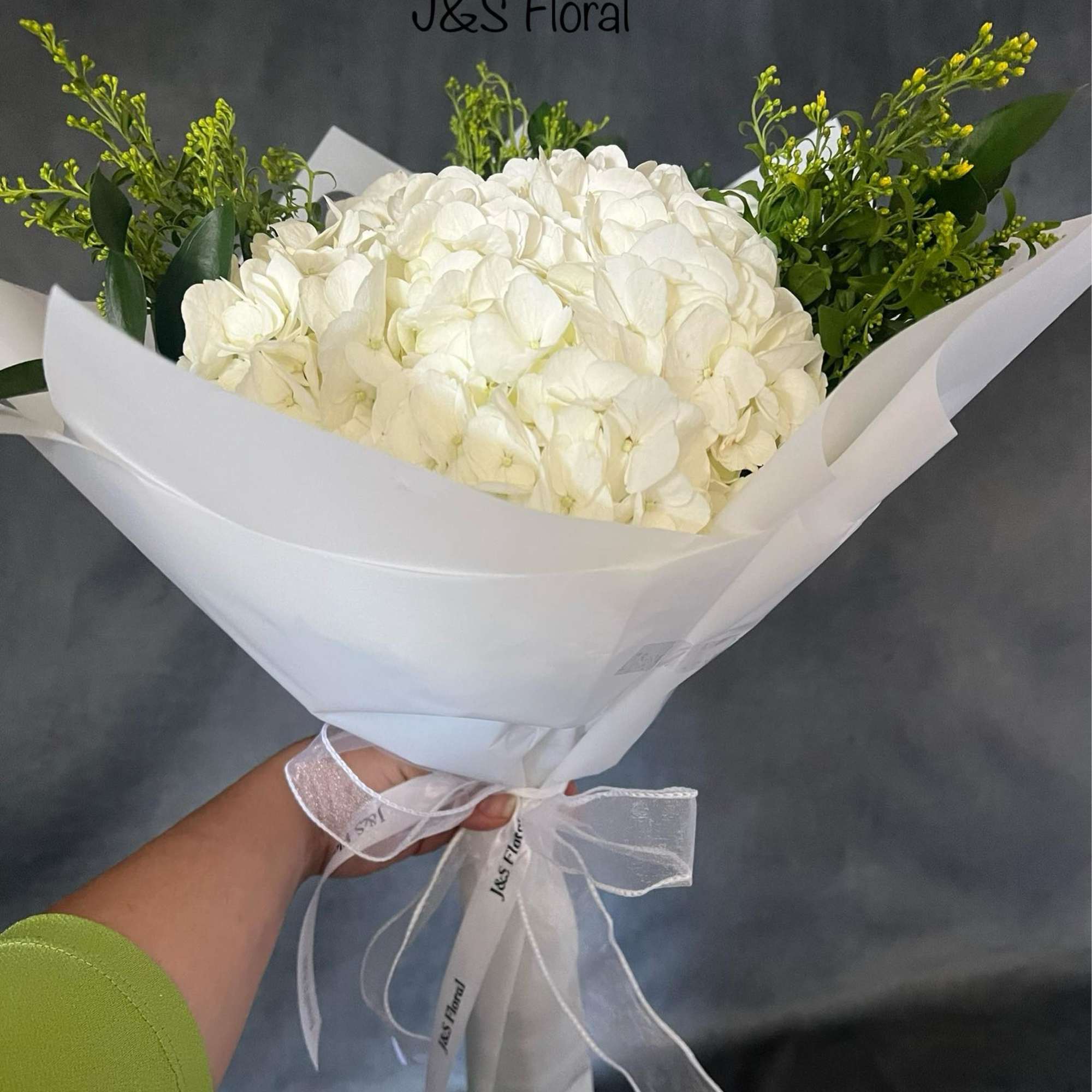 White hydrangea bouquet wrapped in white paper with green accents