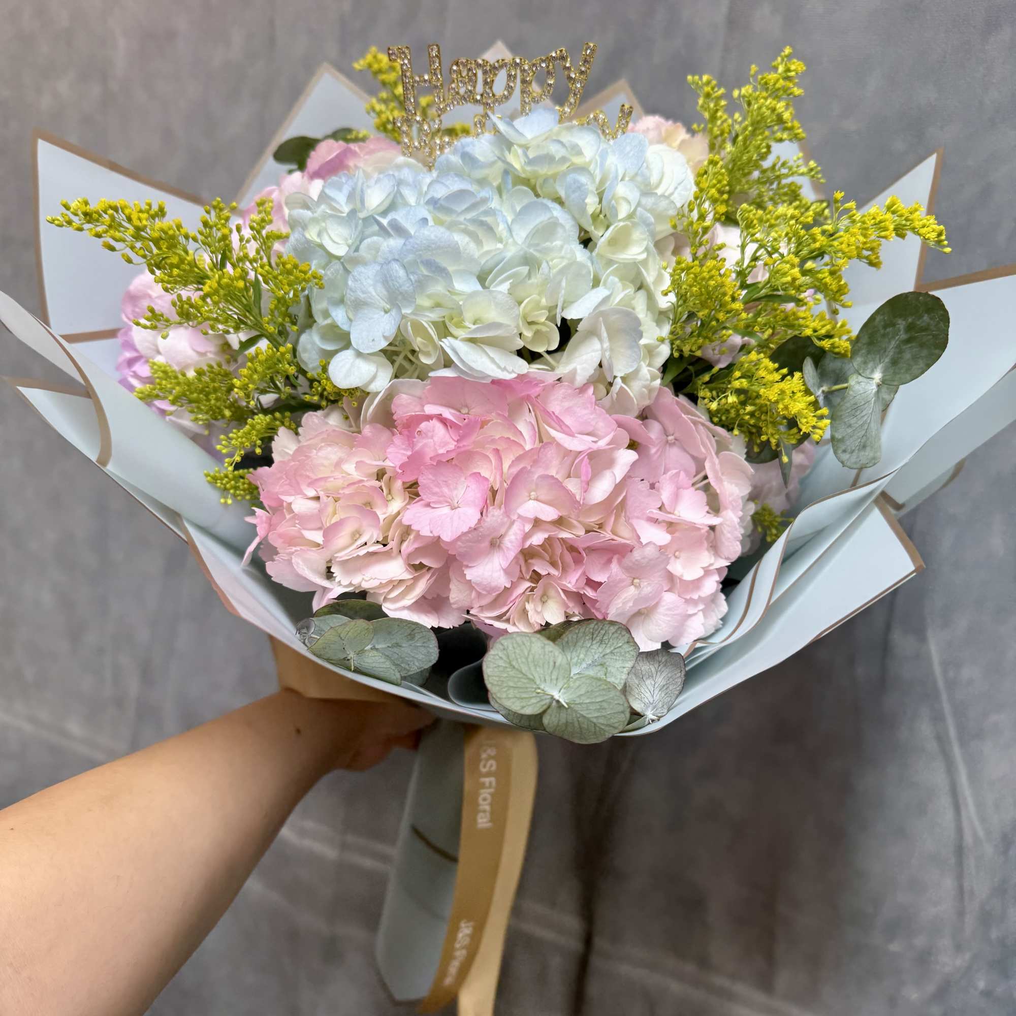 Pink and blue hydrangea bouquet with yellow filler and a glittery topper