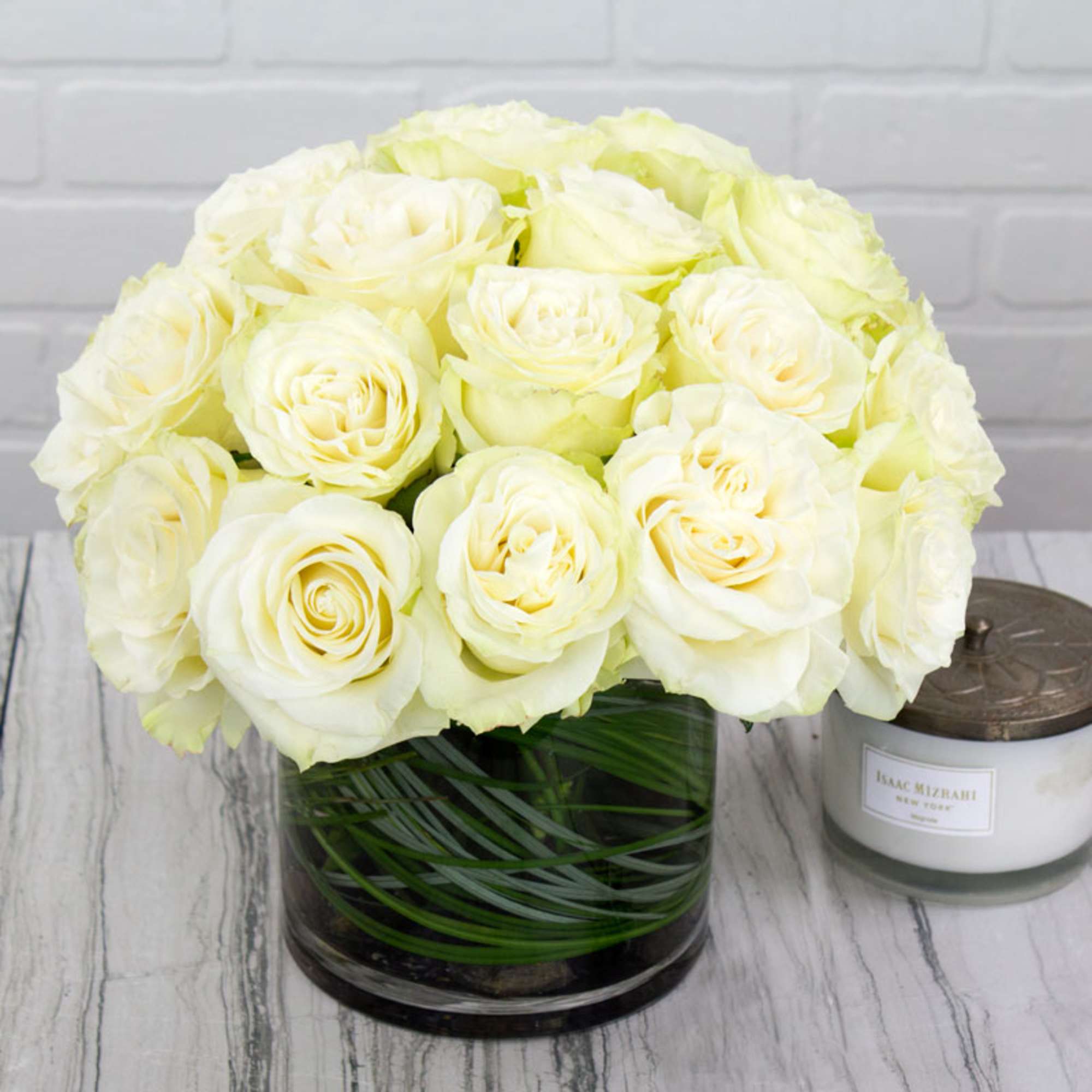 Bouquet of cream-white roses in a clear glass vase beside a candle jar