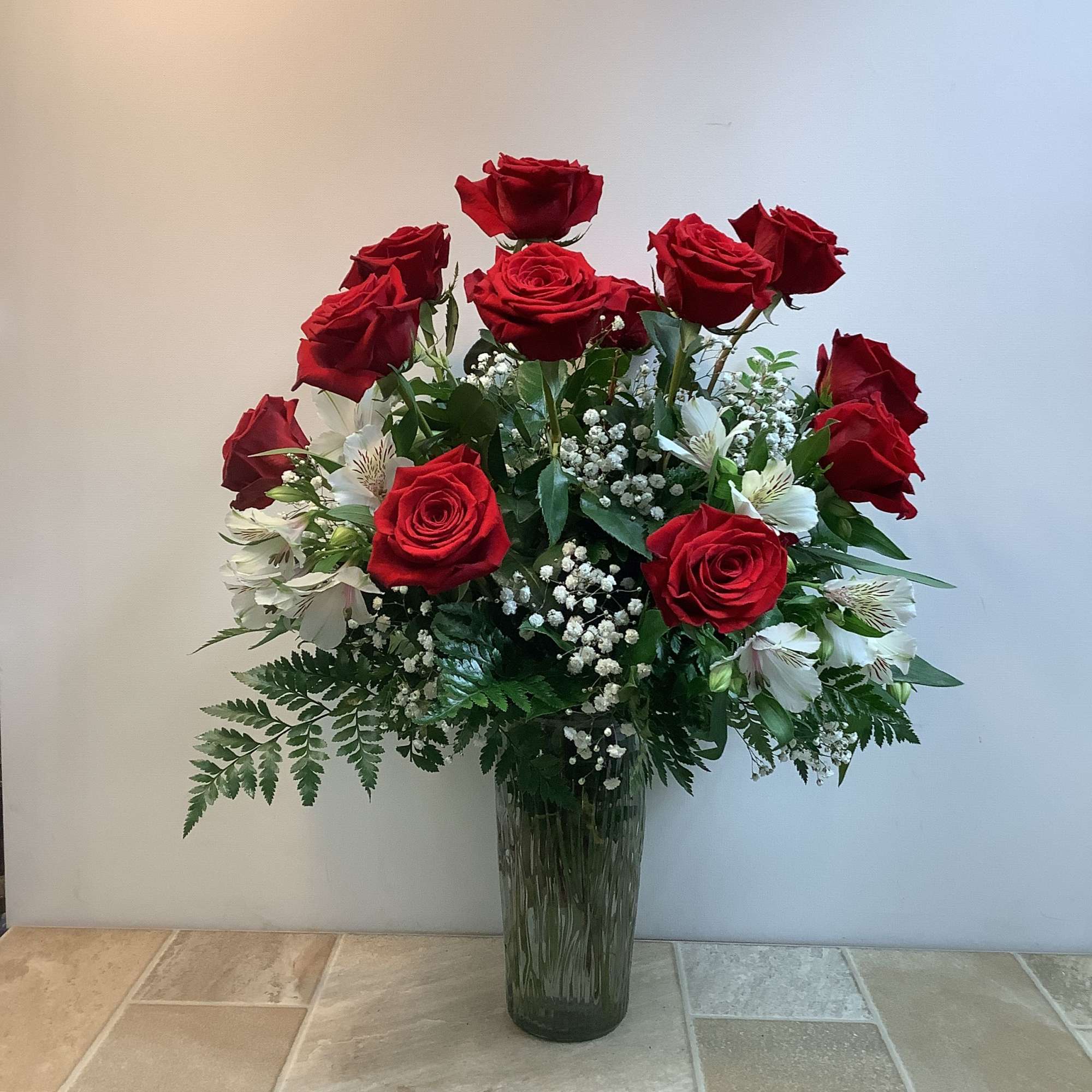 Red roses and white flowers arranged in a tall glass vase.