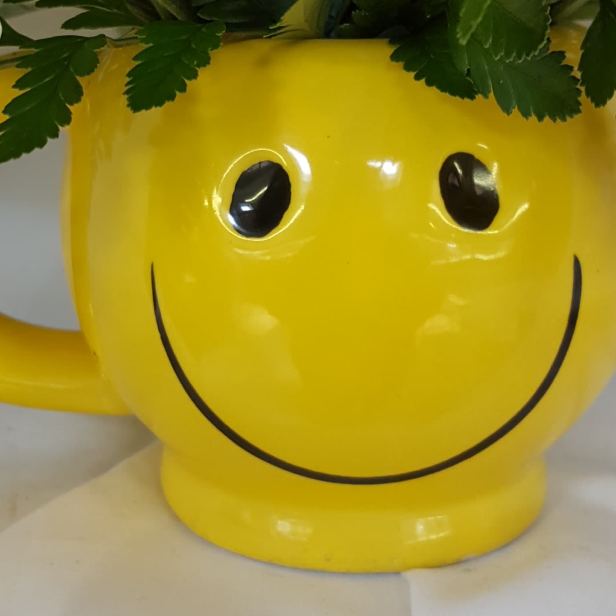 Yellow smiley-face mug holding white flowers and greenery