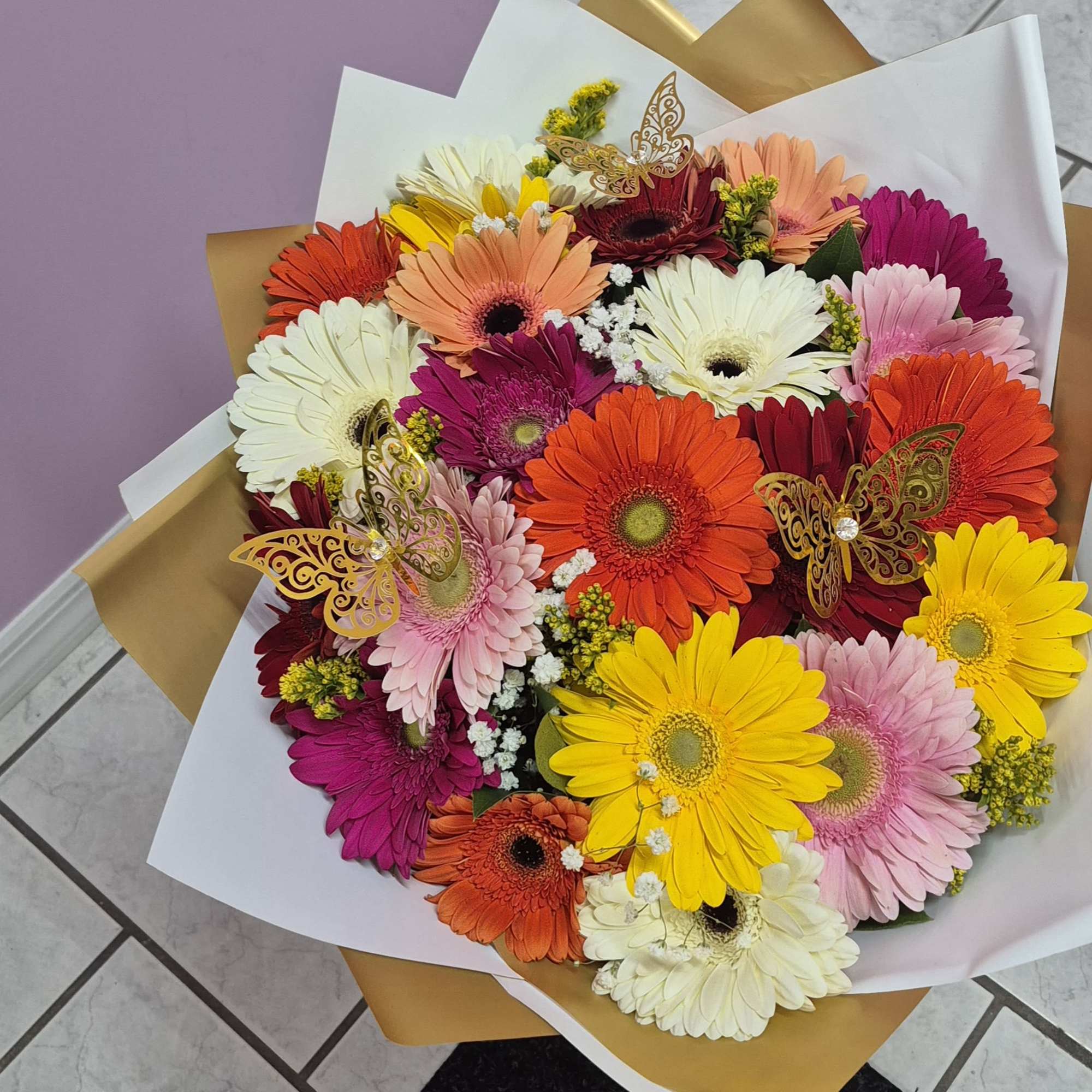 Colorful bouquet of gerbera daisies wrapped in white and gold paper