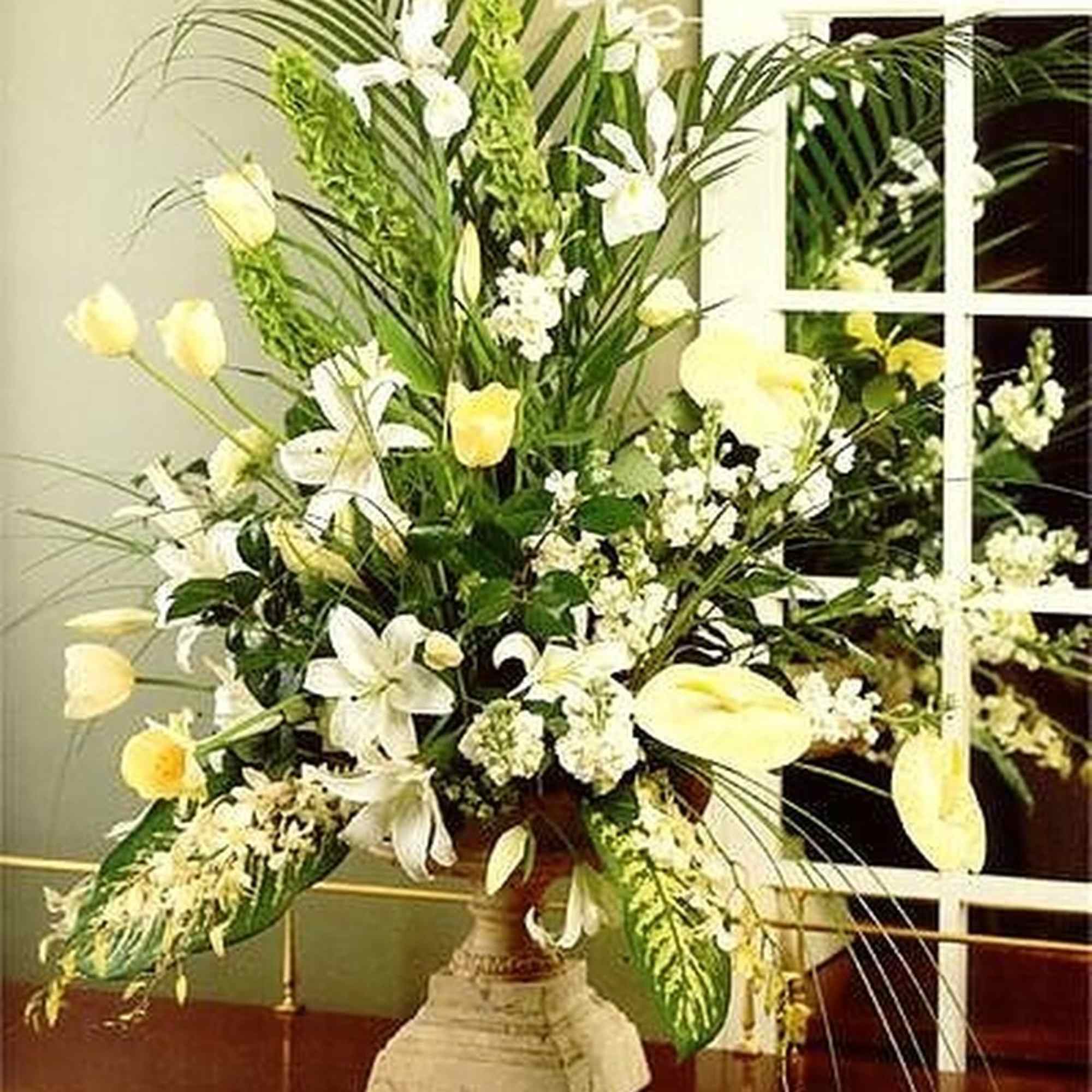 Tall arrangement of white and pale yellow flowers in a stone urn vase