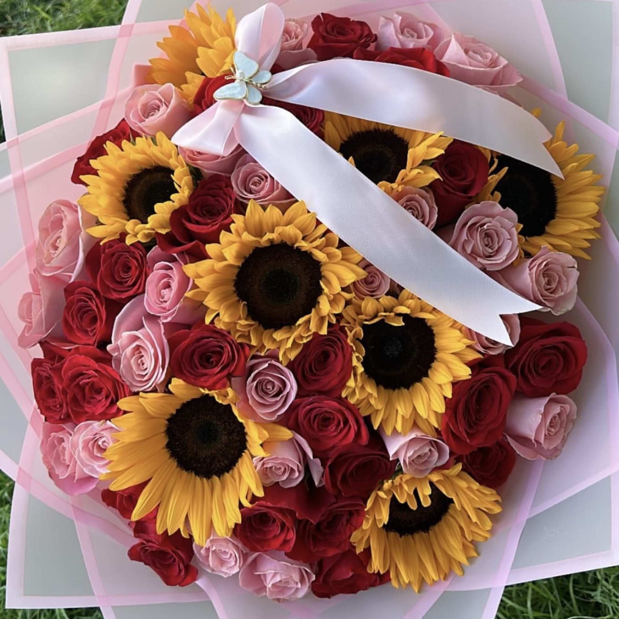 Bouquet of red and pink roses with sunflowers, wrapped in pink paper and tied with a white ribbon