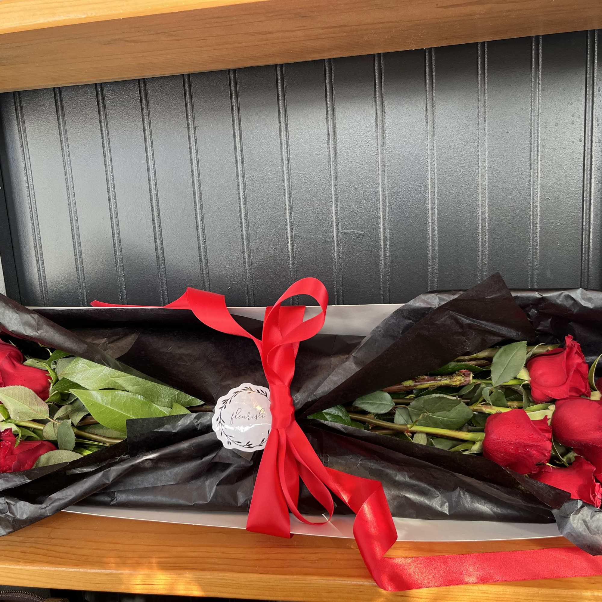 Two bouquets of red roses wrapped in black paper with a red ribbon