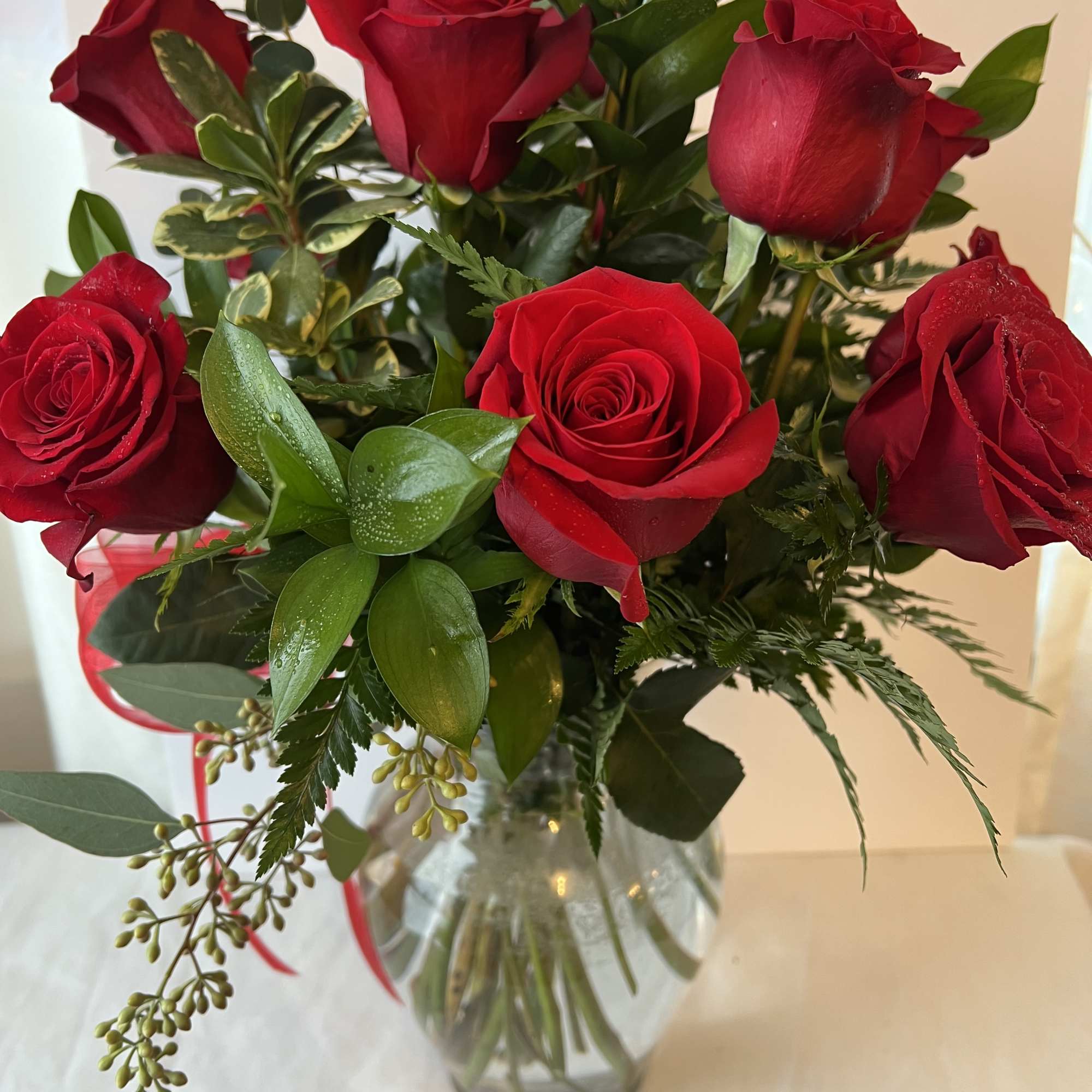 Red roses arranged in a clear glass vase with mixed greenery