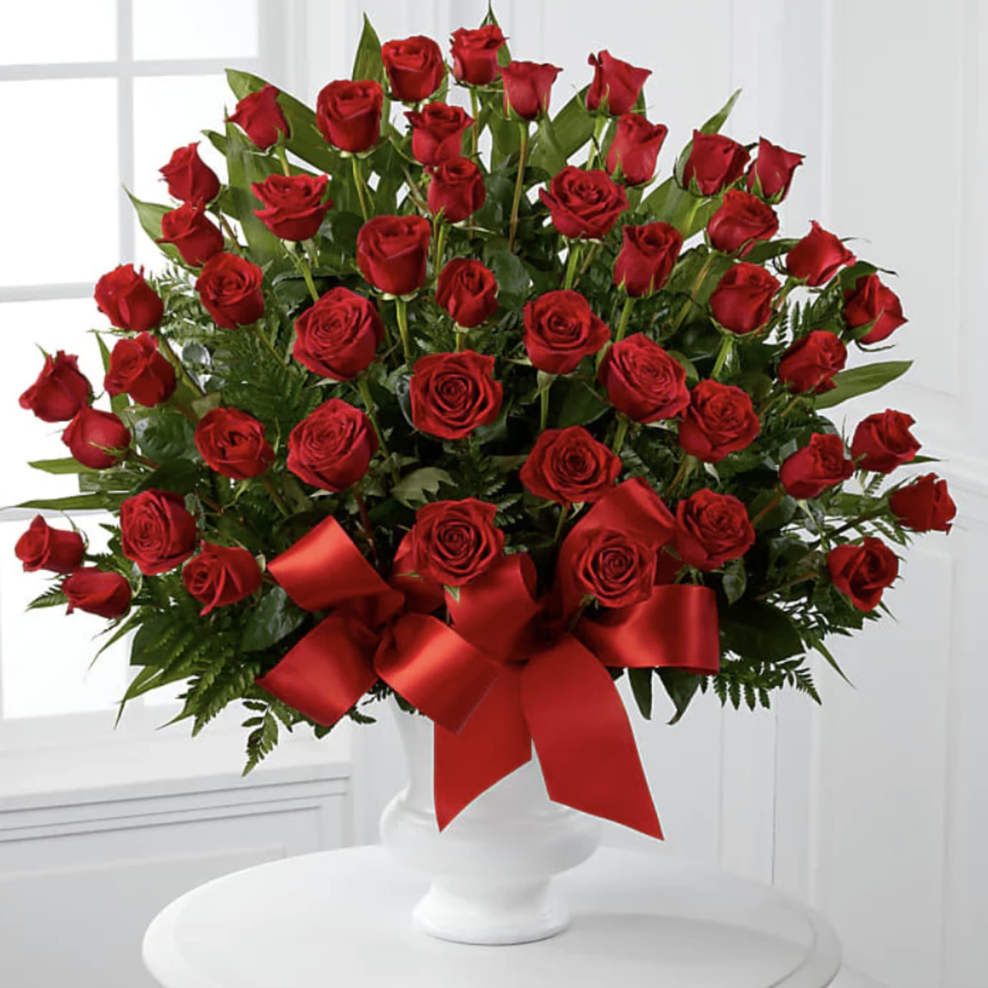 Large bouquet of red roses in a white vase with a red ribbon