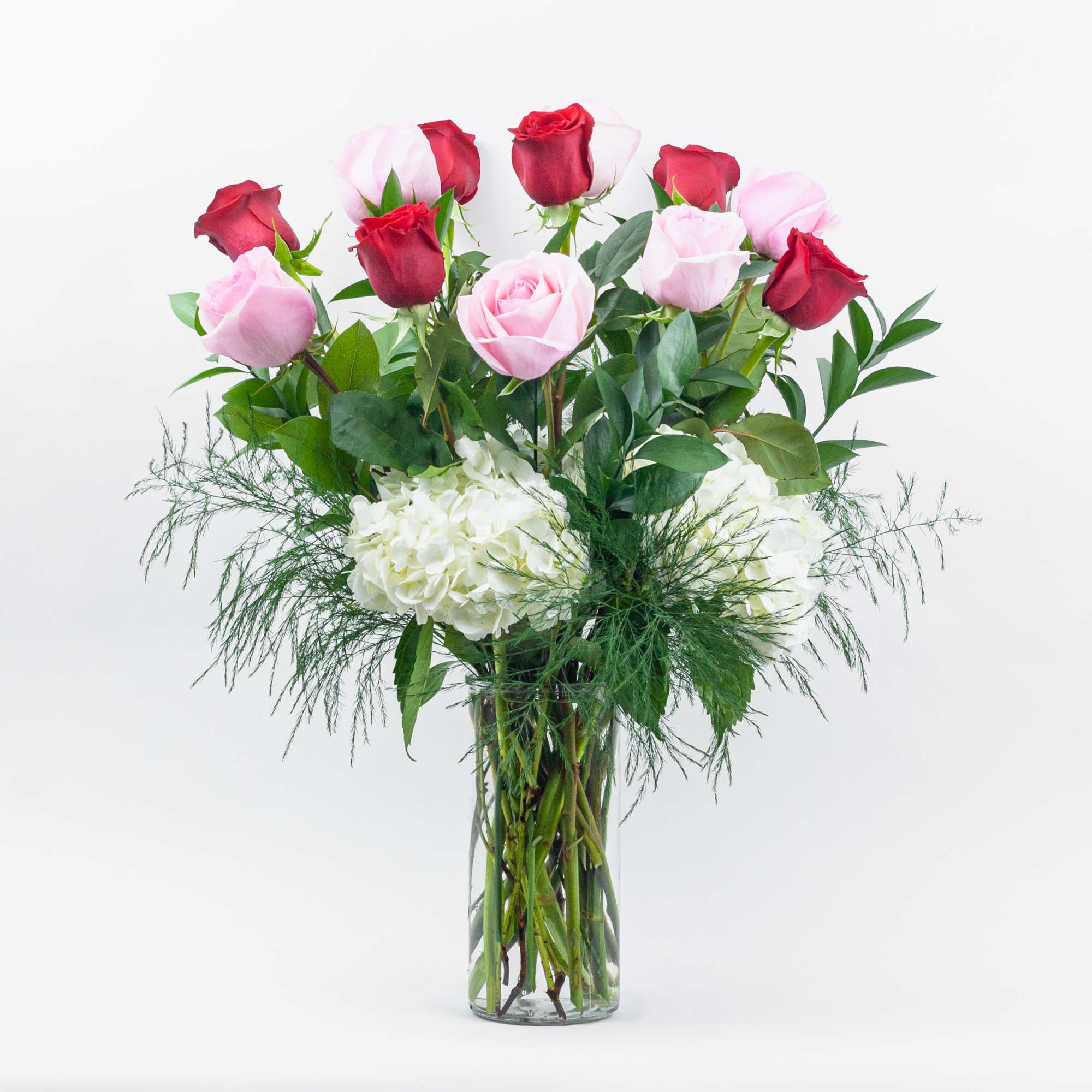 Pink and red roses in a clear glass vase with white hydrangeas