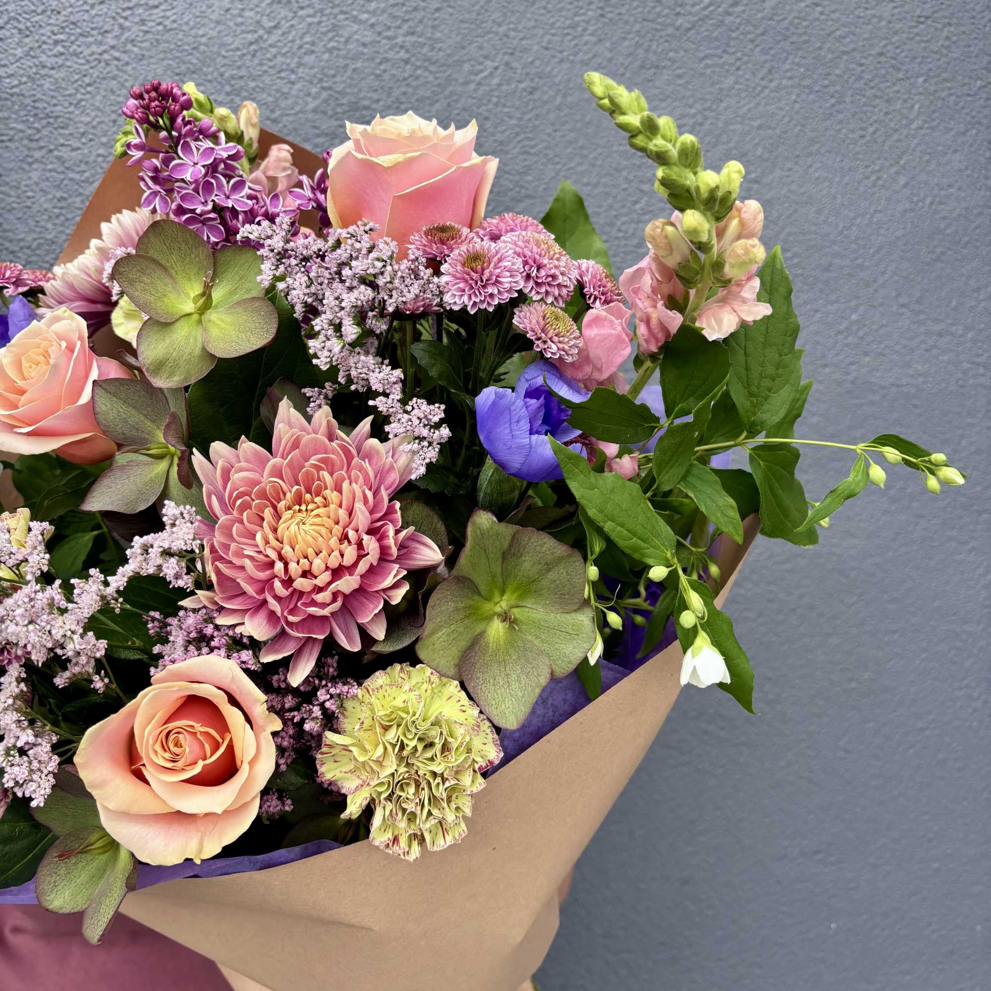Wrapped bouquet of pink roses, chrysanthemums, and mixed blooms in soft pastel tones