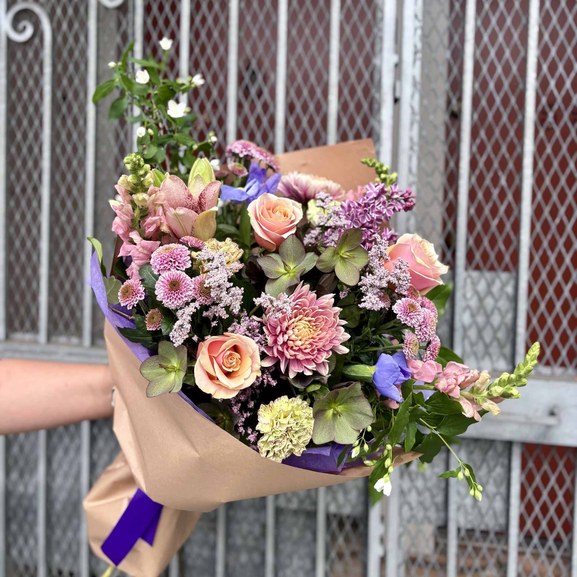 Hand-tied bouquet of pink and peach flowers wrapped in kraft paper with purple accents