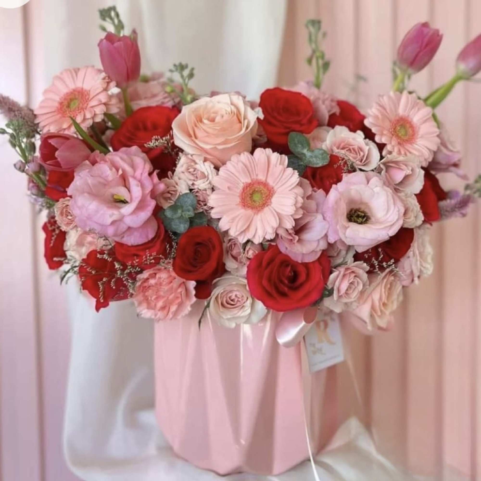 Pink and red bouquet with roses, gerbera daisies, and tulips in a pink wrap