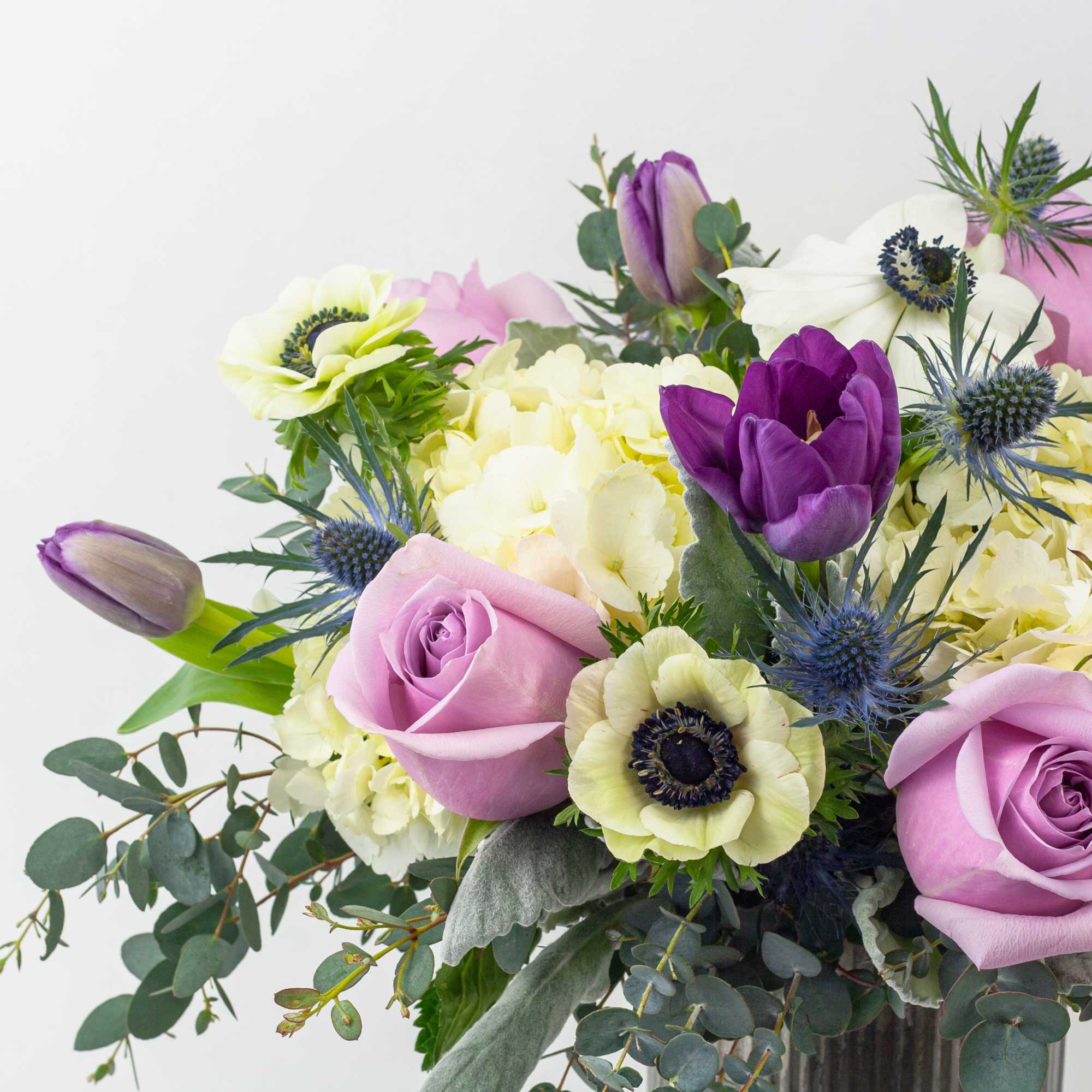 Bouquet of lavender roses, purple tulips, and pale flowers in a vase