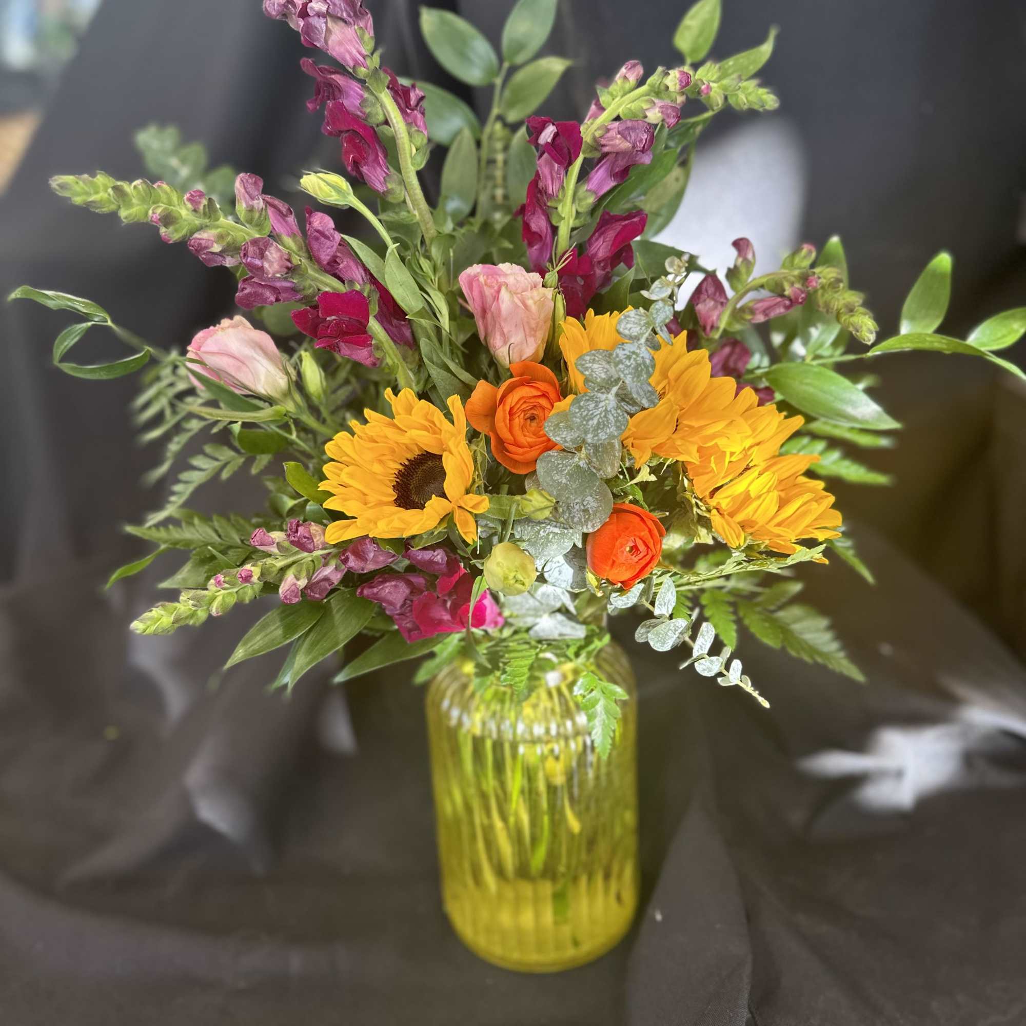 Designed using pinky burgundy snapdragons, sunflowers, pink lisianthus, queen anne's lace, and