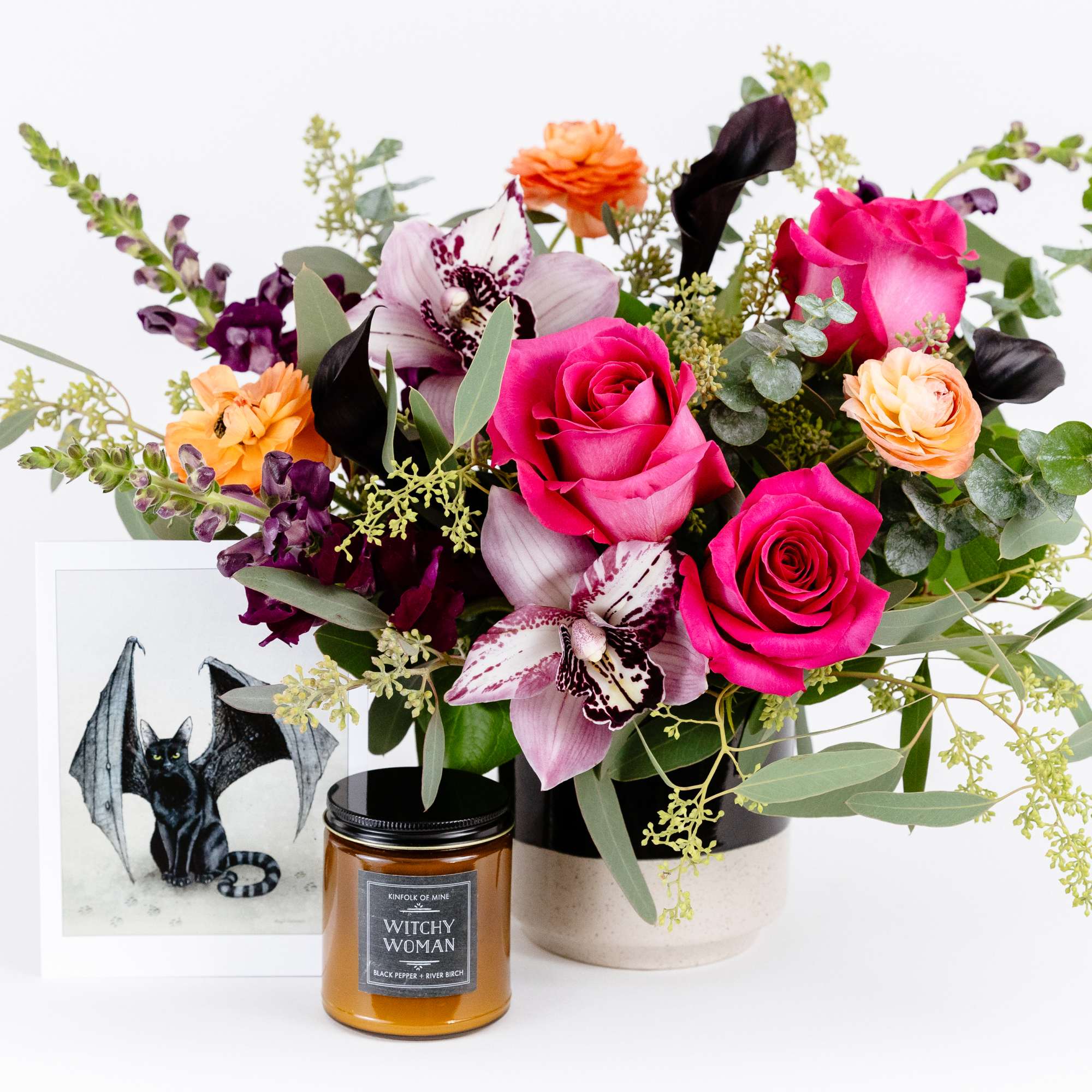Mixed bouquet with pink roses and orchids in a vase beside a candle and framed bat print