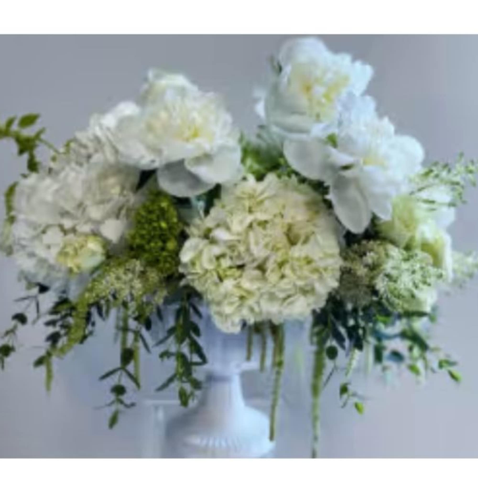 White floral arrangement in a pedestal vase with trailing greenery