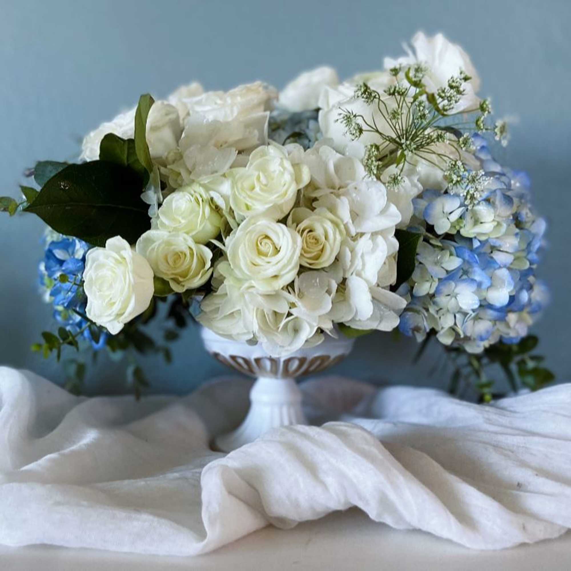 White roses and blue hydrangeas arranged in a white pedestal vase