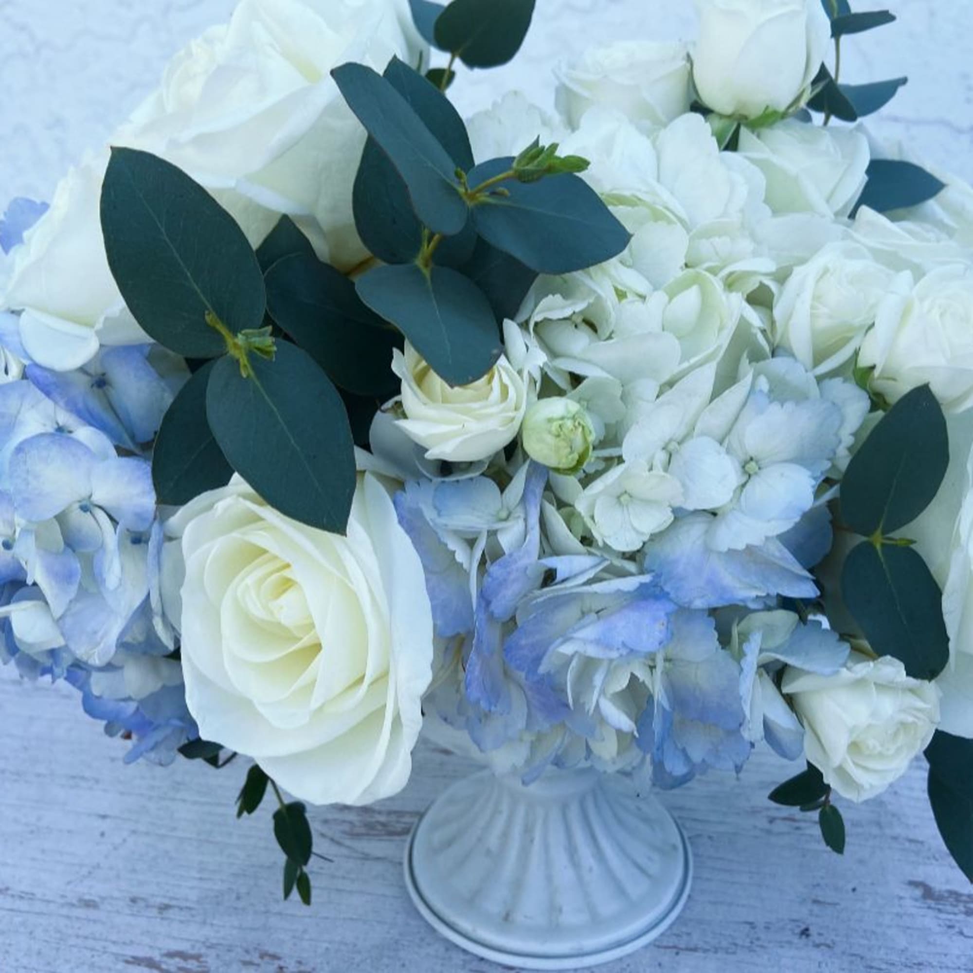 White roses and pale blue hydrangeas in a white vase