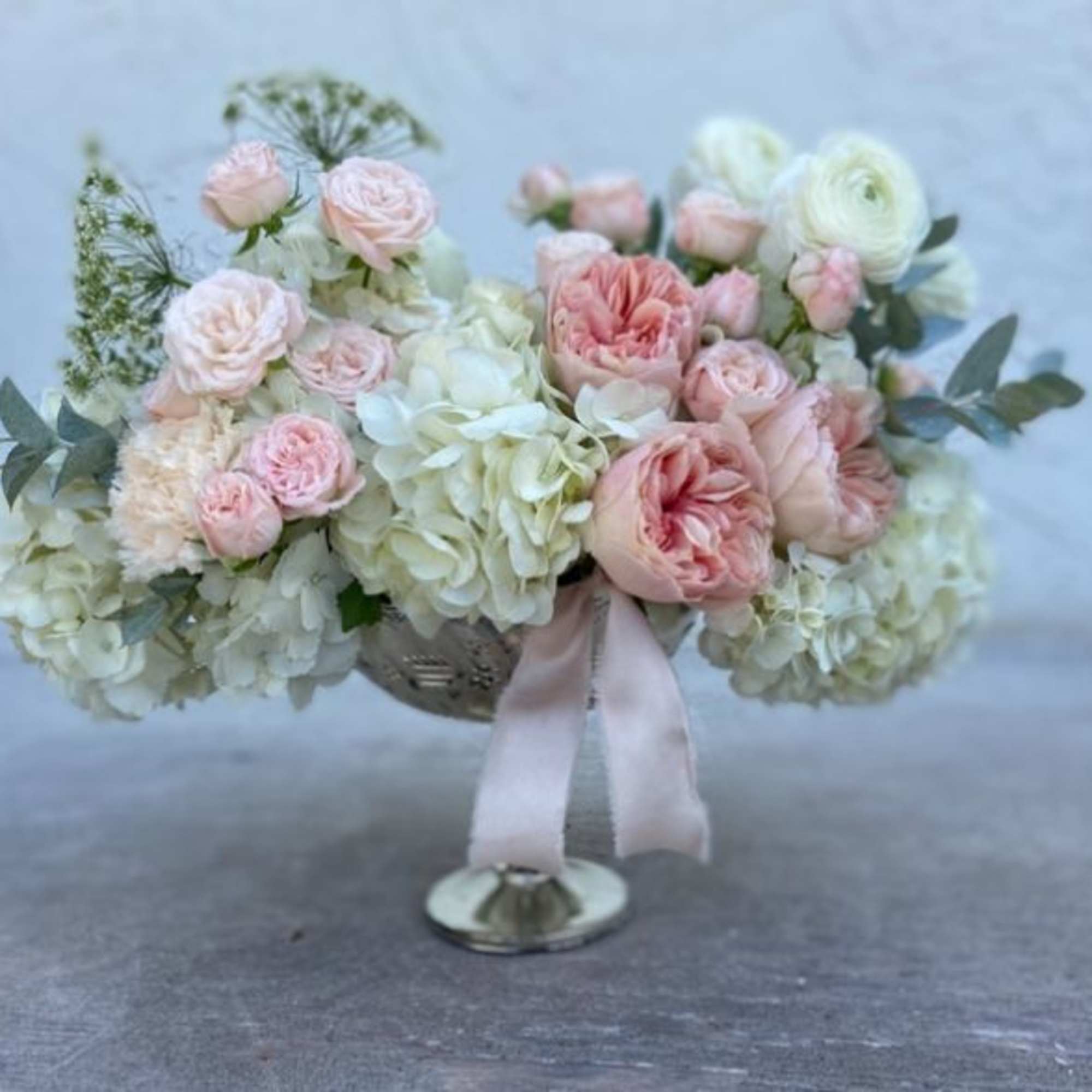 Pink and white floral arrangement in a silver pedestal vase with a ribbon