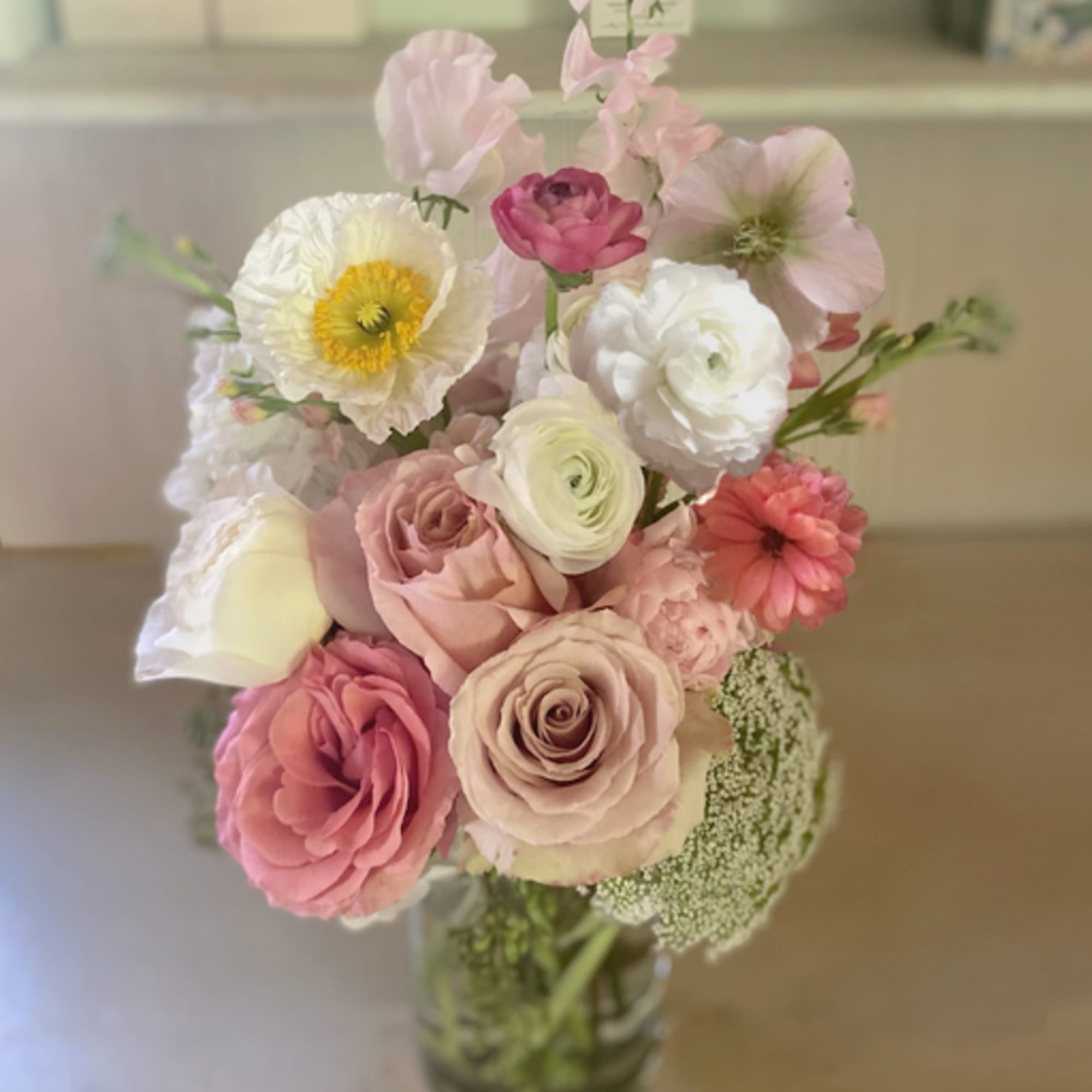 Tall bouquet of pink roses, white ranunculus, and mixed pastel blooms in a clear glass vase