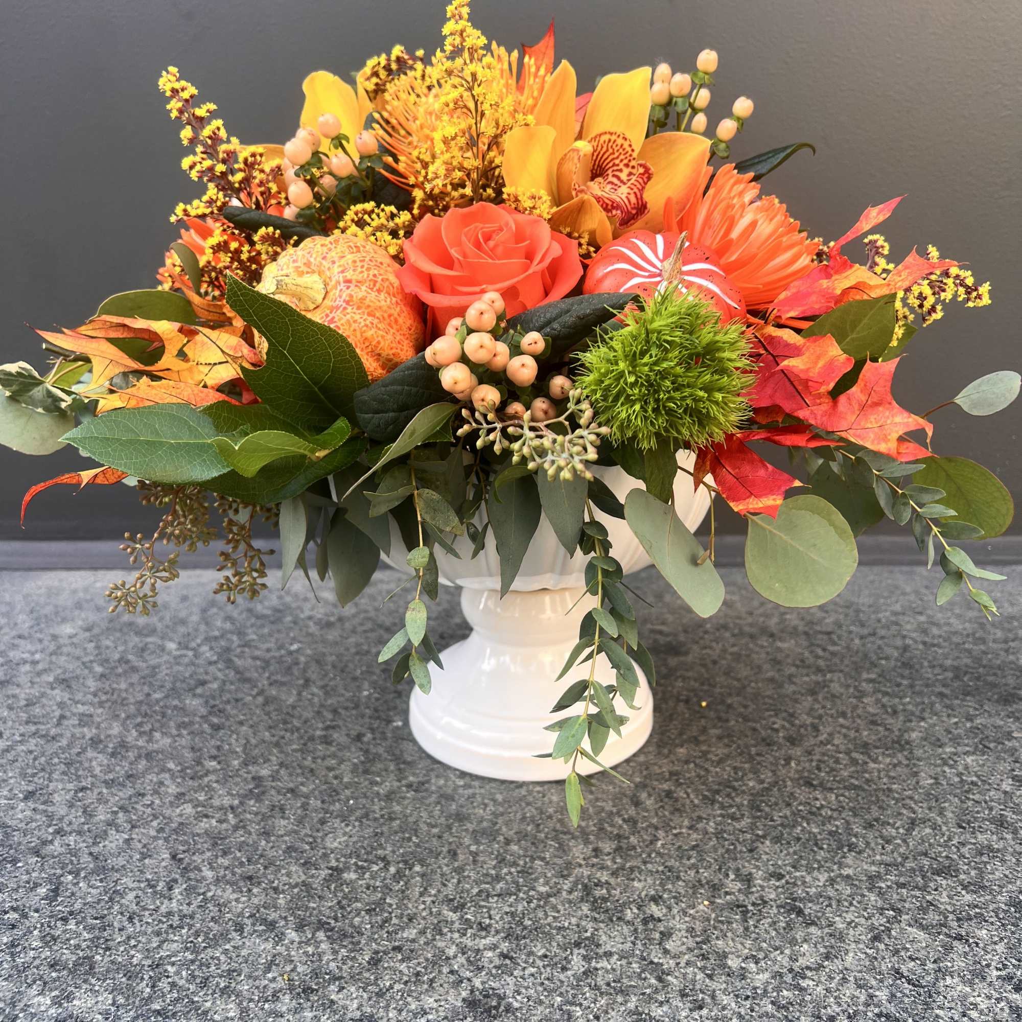 Autumn floral arrangement in a white vase with orange and yellow blooms
