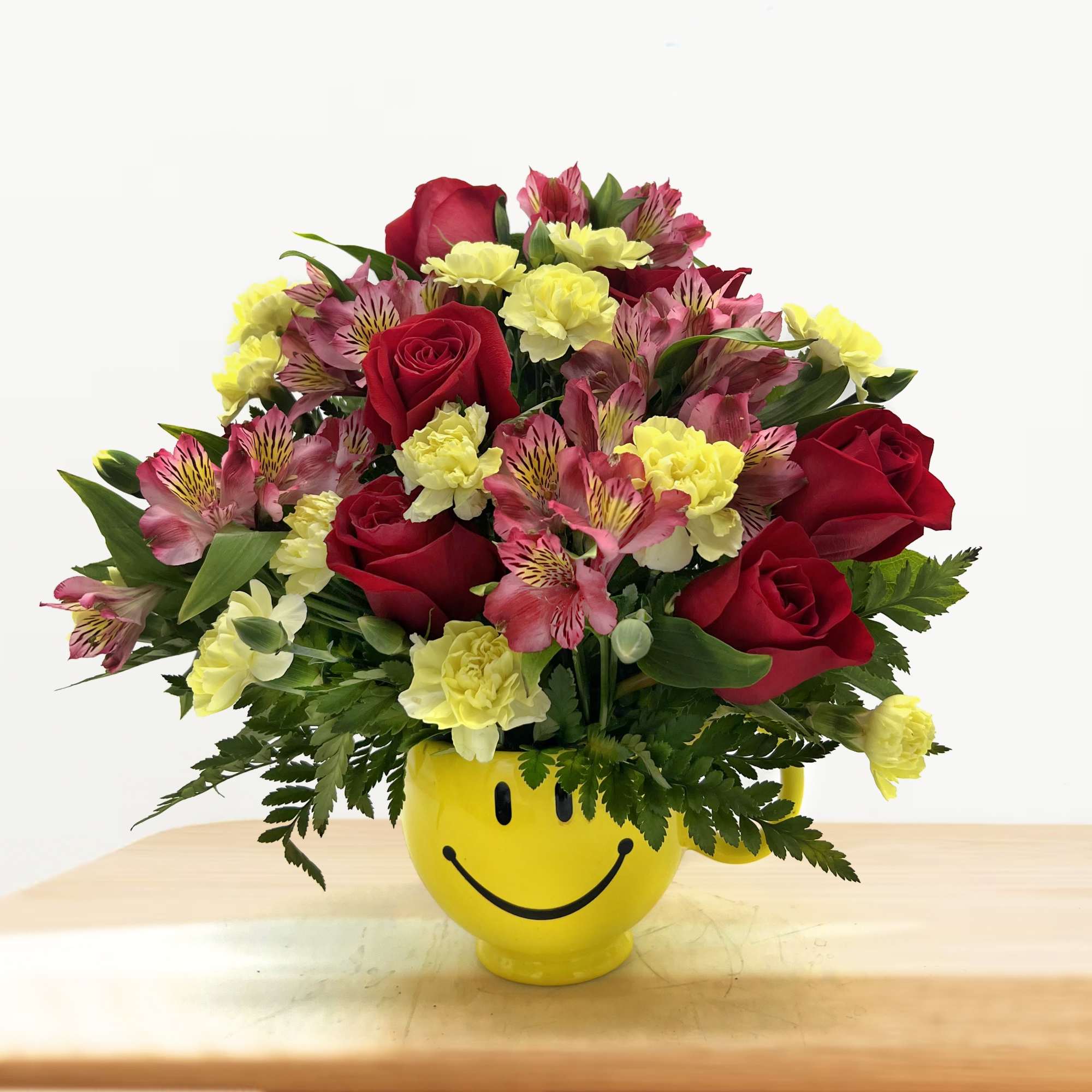 Bouquet of red roses, pink alstroemeria, and yellow carnations in a smiley-face mug